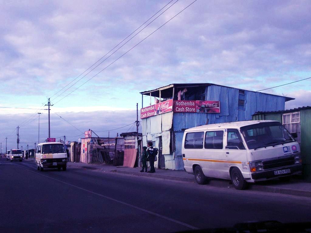 Minibus taxis parked outside a corrugated-iron cash store at dawn in a township street