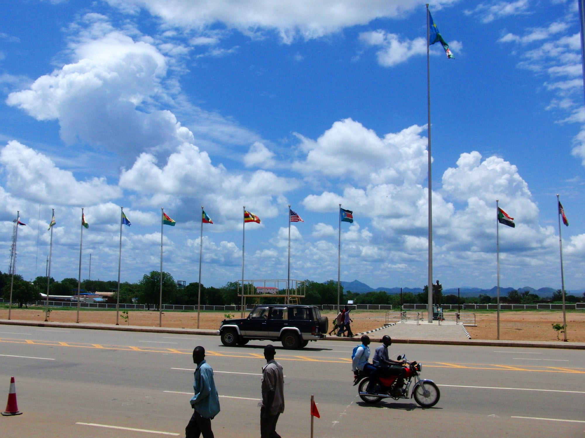 A wide city street lined with national flags, traffic passing beneath a big sky