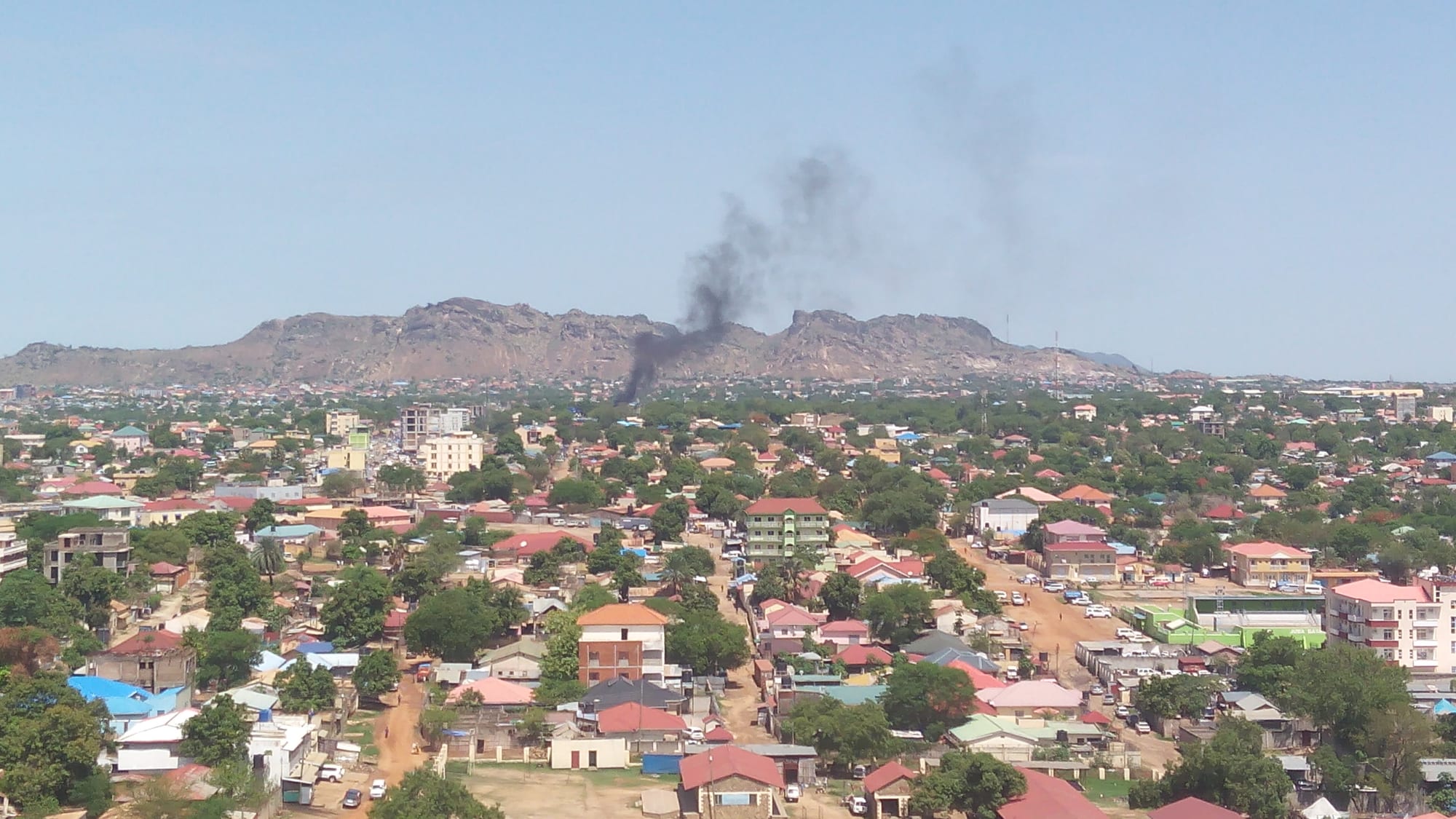 Low-rise buildings, dusty roads and green trees of Juba seen from a rise, with the White Nile beyond