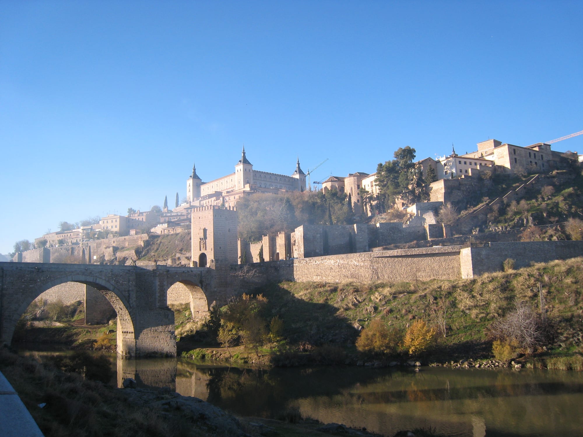 A hilltop medieval city with a stone bridge crossing the river below