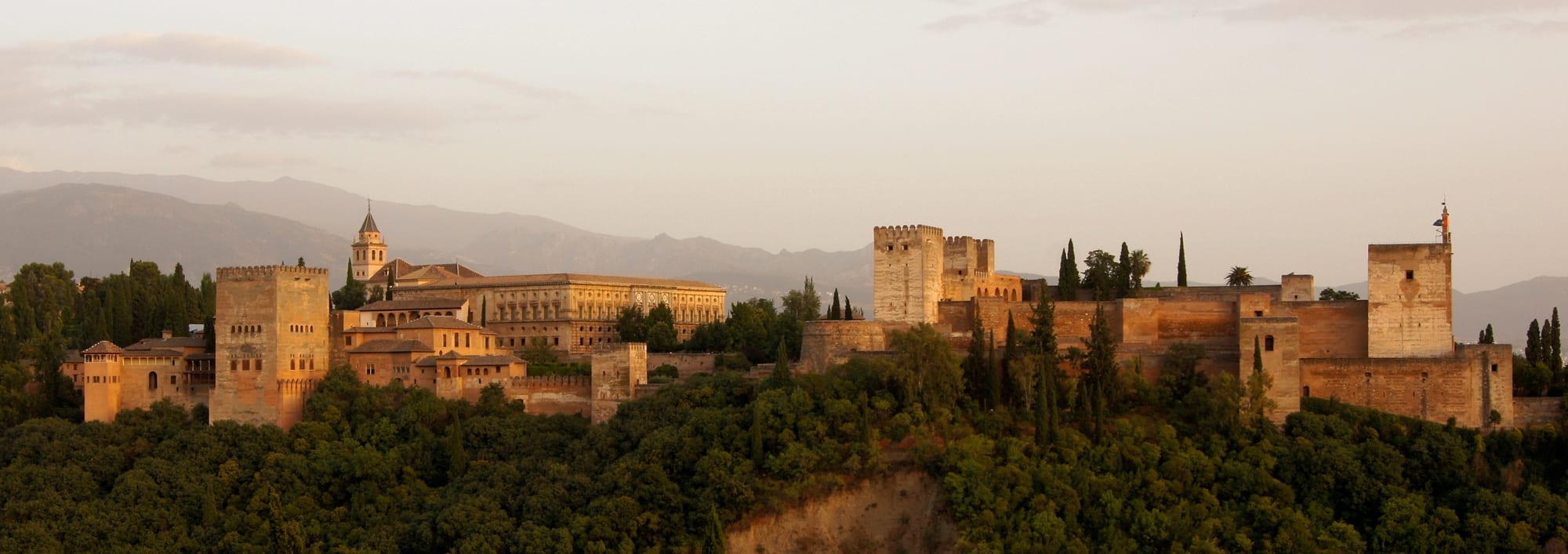 The reddish walls and towers of the Alhambra palace-fortress on a hill above Granada with the Sierra Nevada behind