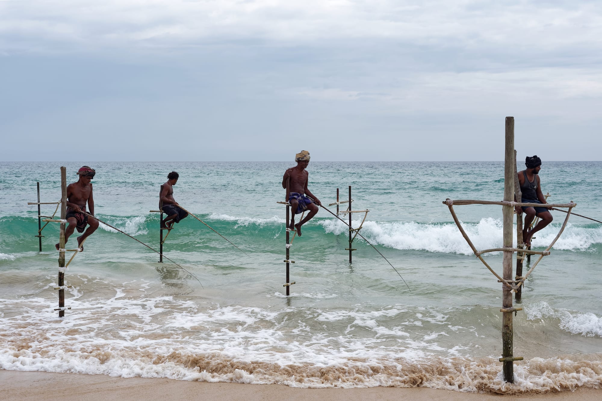 Four fishermen perched on wooden poles set in the surf off Sri Lanka's southern coast, fishing rods extended over the waves