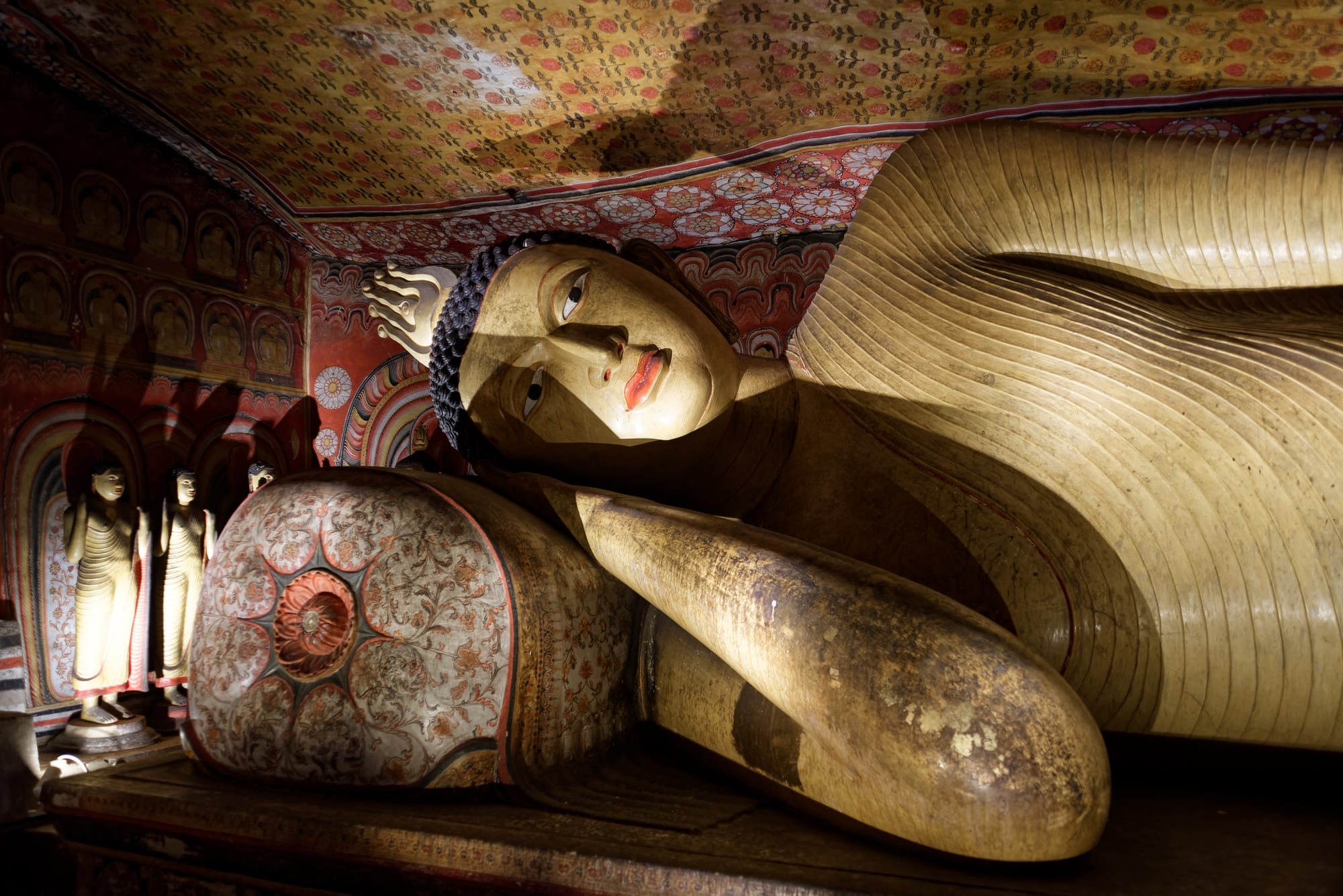 A giant golden reclining Buddha statue inside an ornately painted cave temple