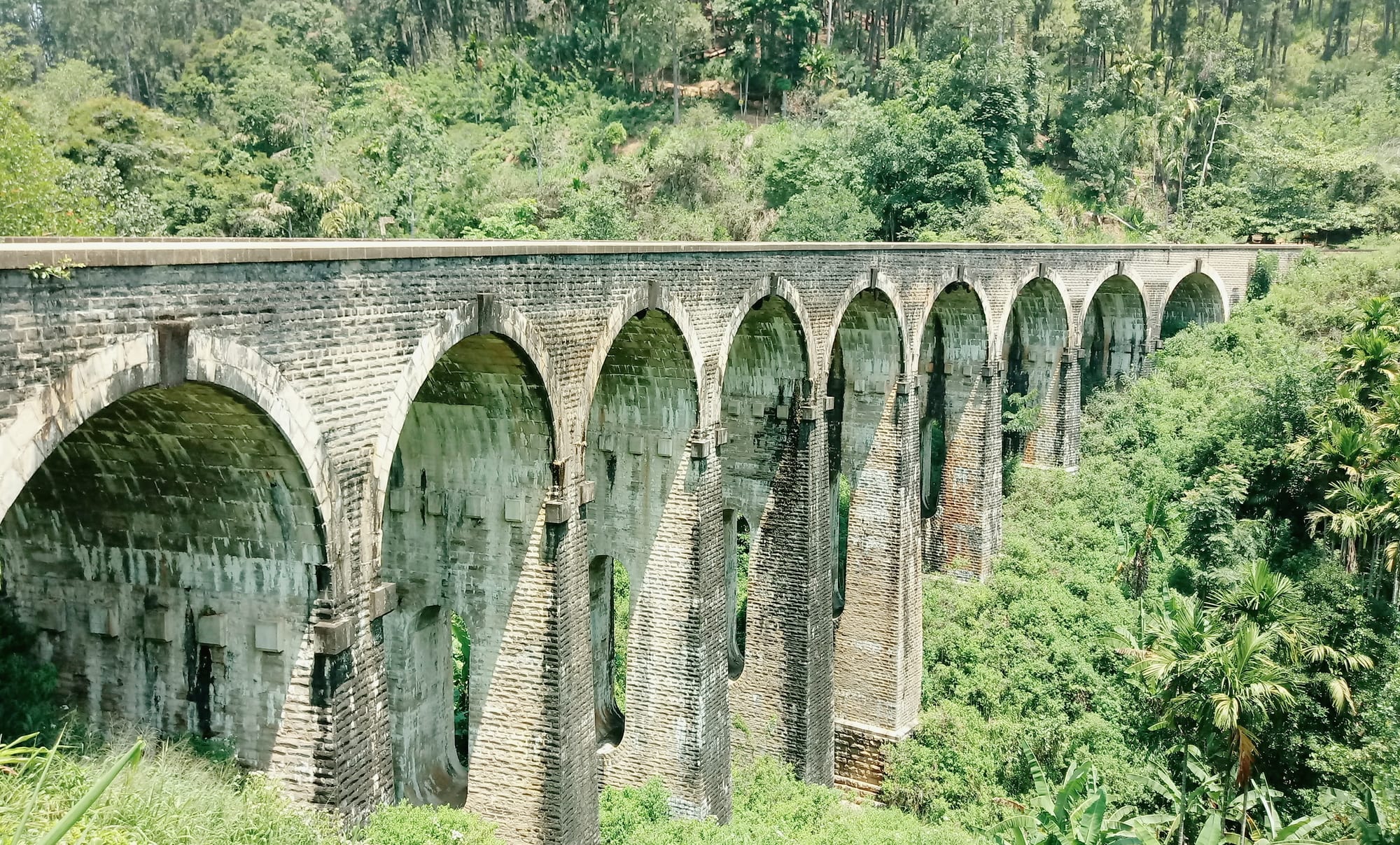 A colonial-era stone railway viaduct with nine arches crossing a green valley