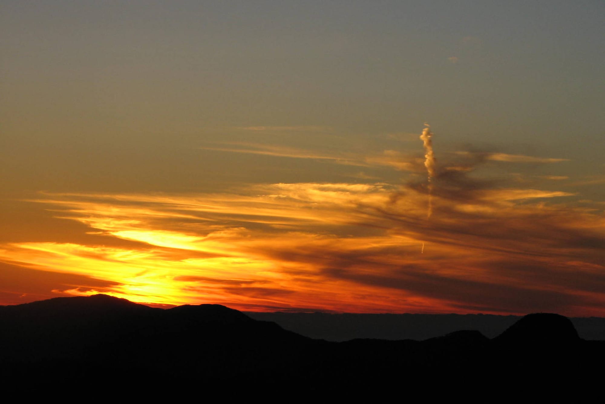 A fiery sunset sky over layered mountain ridges