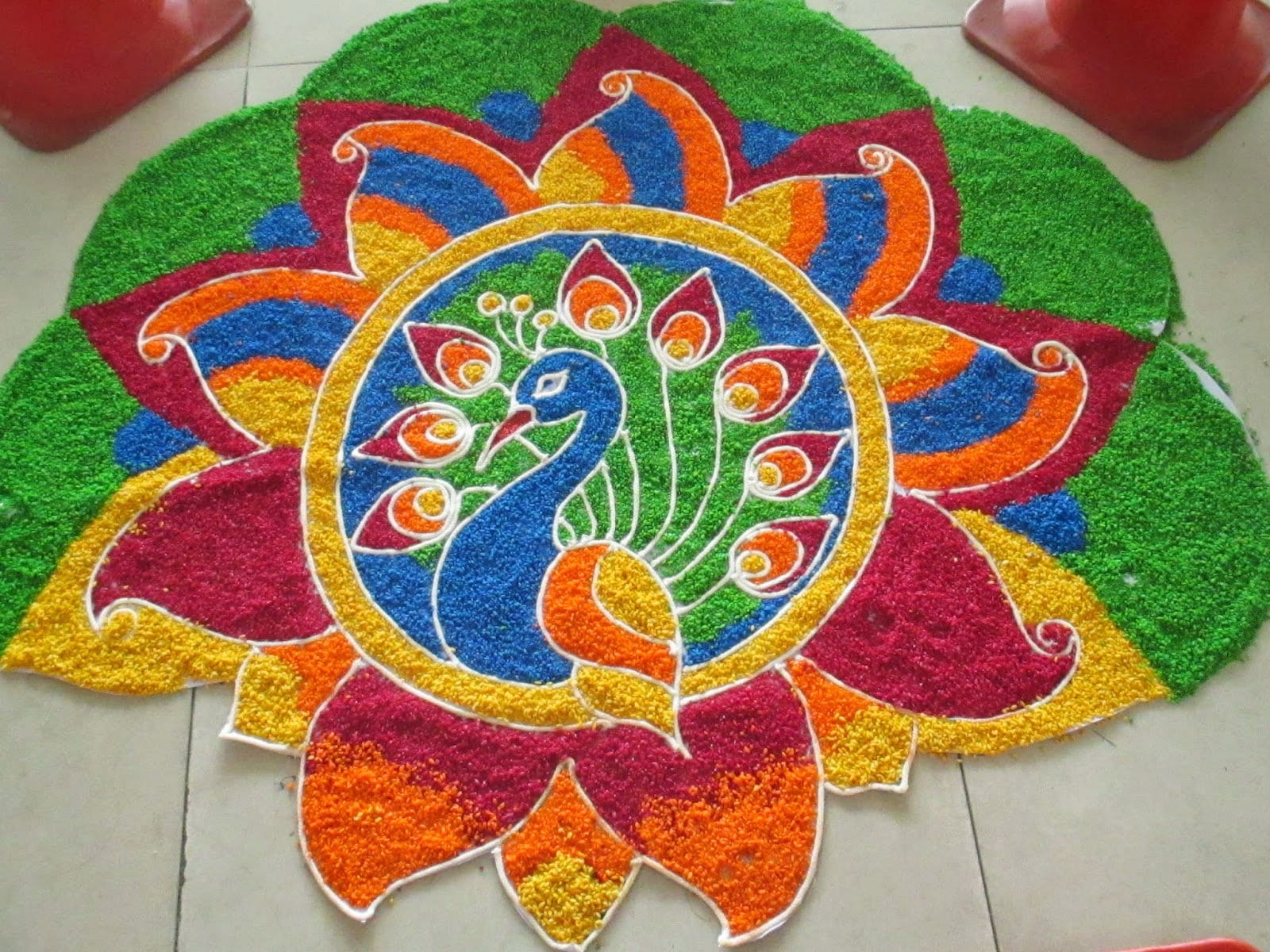 A large floor design made of brightly coloured grains in green, red, blue, orange and yellow, with a blue peacock inside a circle at its centre, surrounded by petal shapes