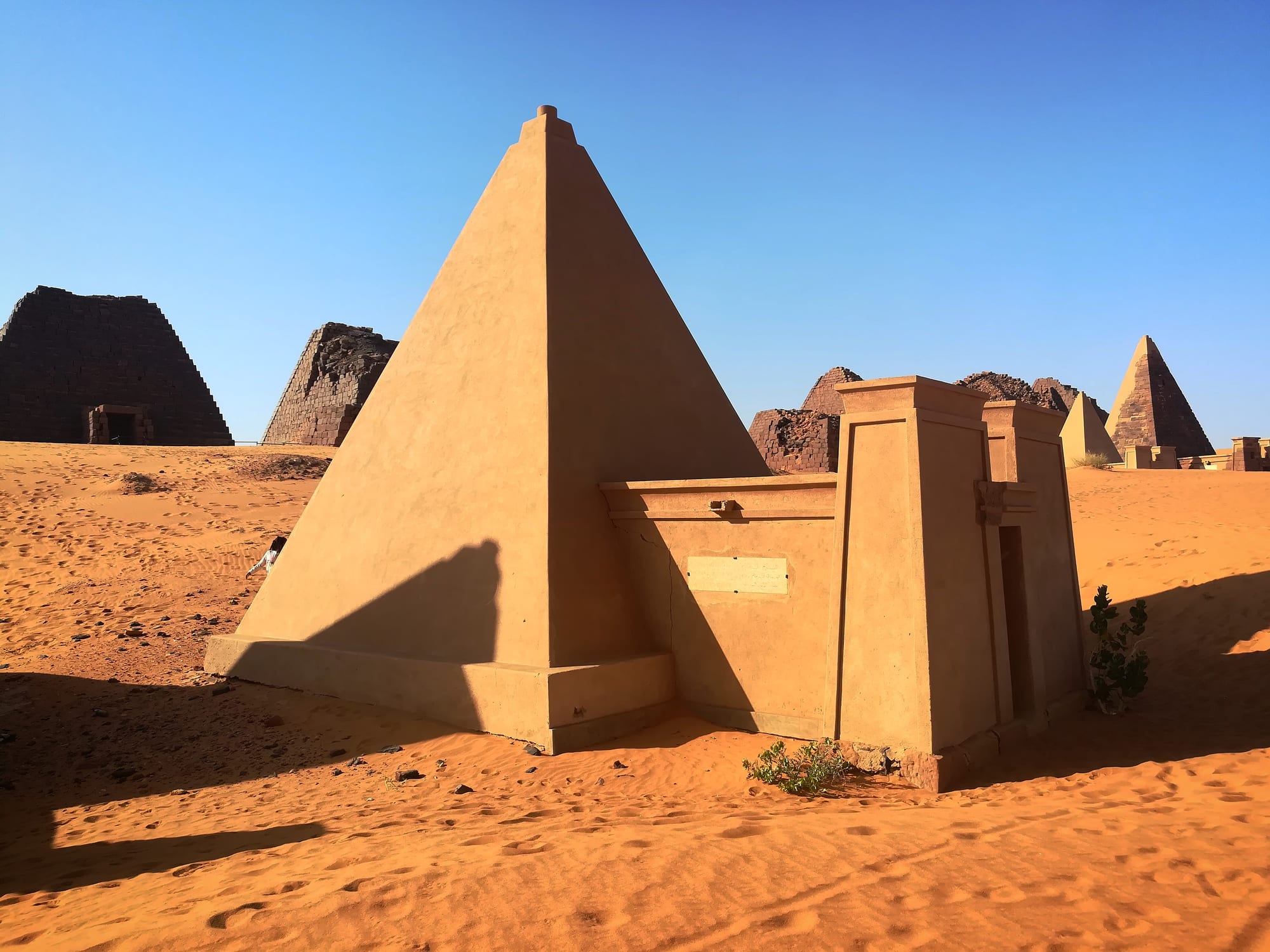 A steep desert pyramid with smaller ruined pyramids visible behind it