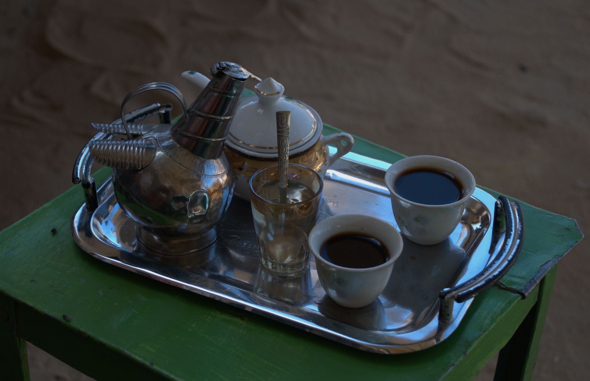 A metal coffee pot, two small cups of dark coffee, a glass of water and a sugar bowl arranged on a tray in Wadi Halfa, Sudan