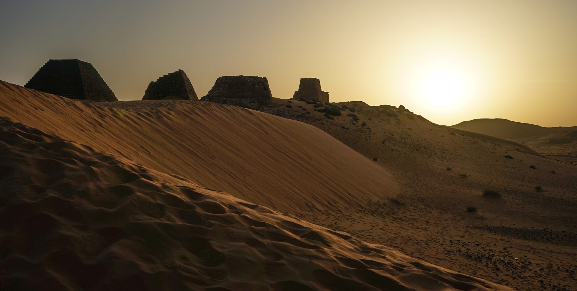 A cluster of steep, narrow sandstone pyramids on a desert ridge under a clear sky at Meroë