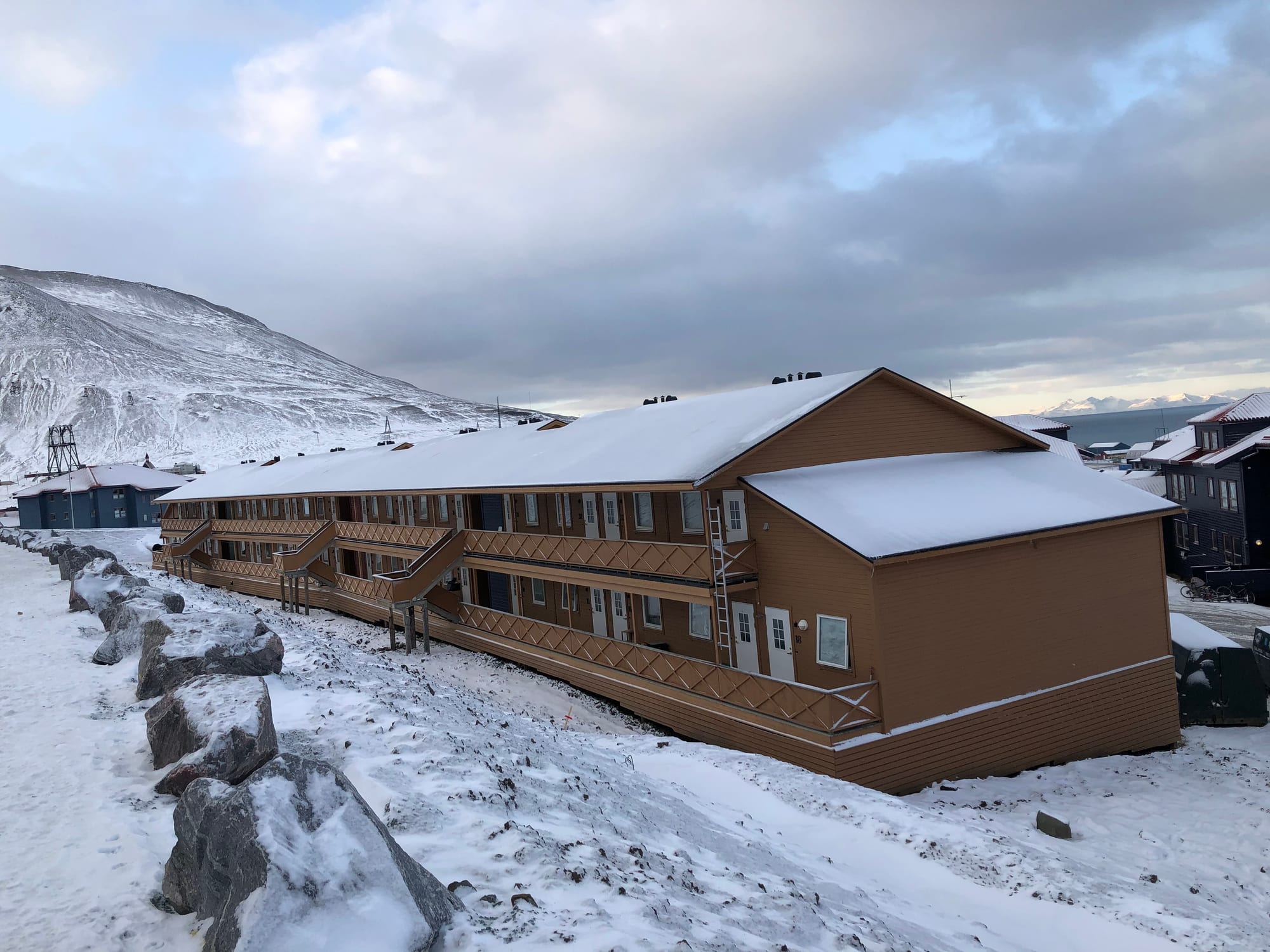 A long terraced housing block in Longyearbyen raised up on metal stilts above the snow-covered ground, a mountain behind