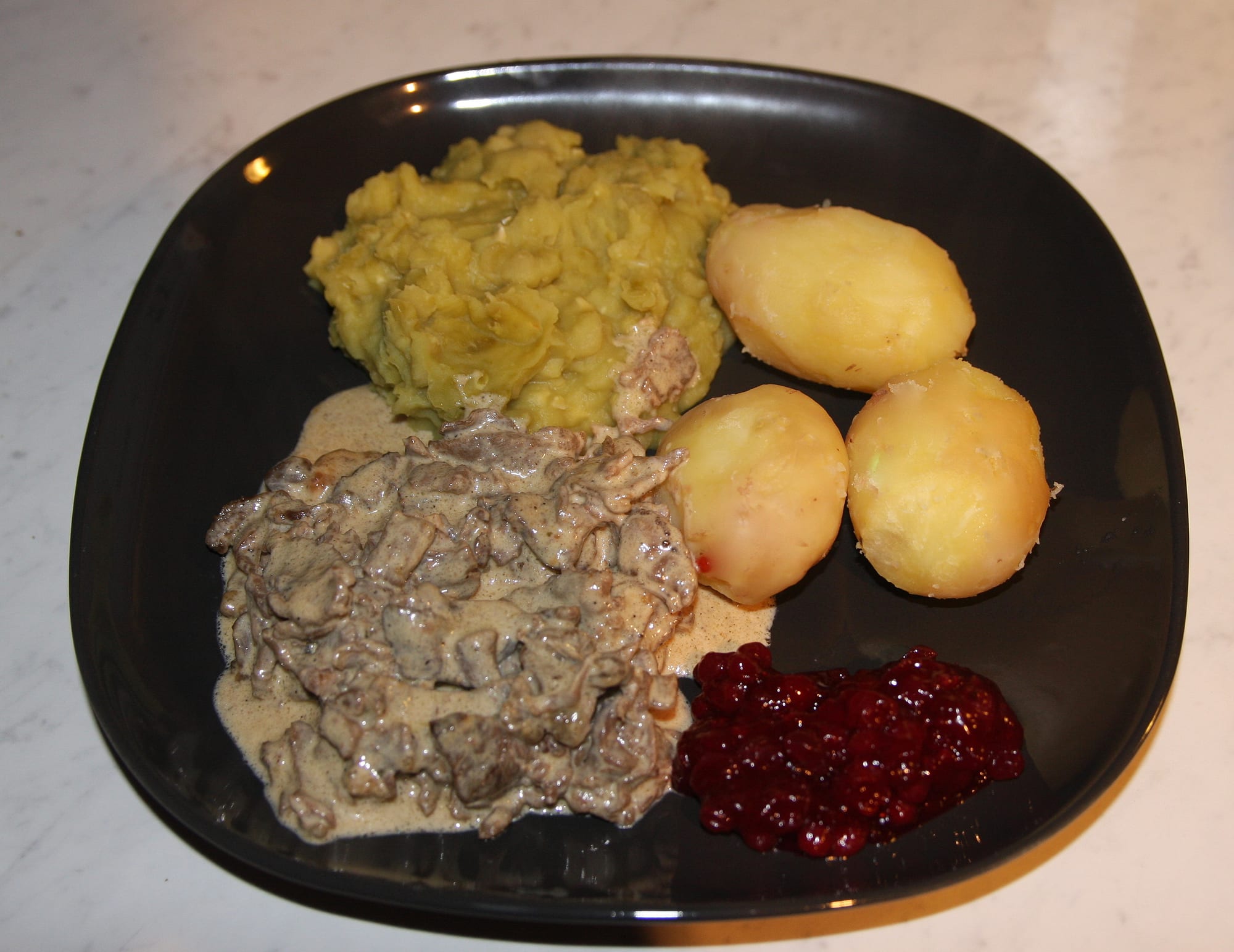 Reindeer meat in a cream sauce served with potatoes, pea stew and lingonberries