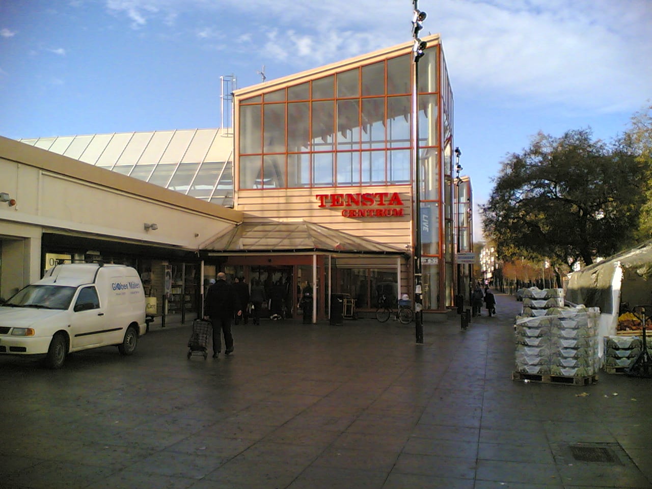 The entrance to a suburban shopping centre called Tensta Centrum, with a van, a cyclist and pedestrians outside