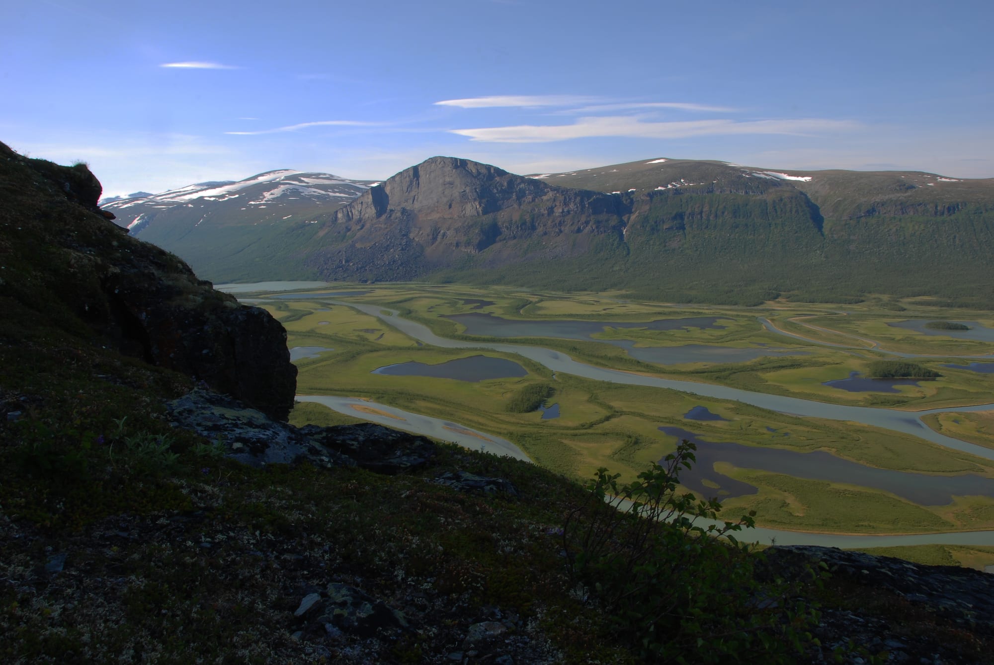 A wide glacial river delta winding through a green valley beneath dramatic mountains