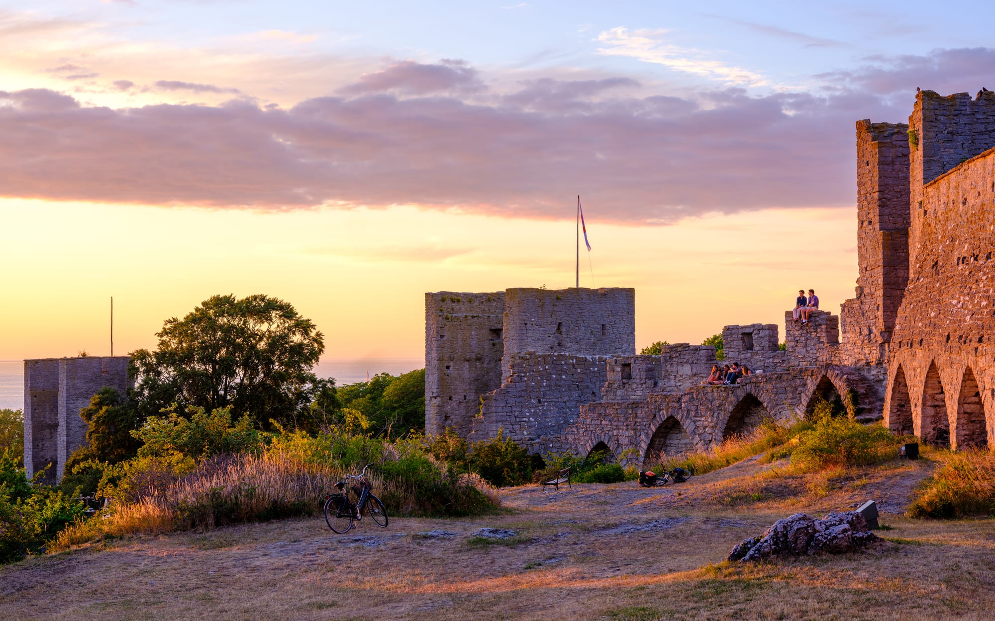 A medieval stone city wall with towers glowing at sunset