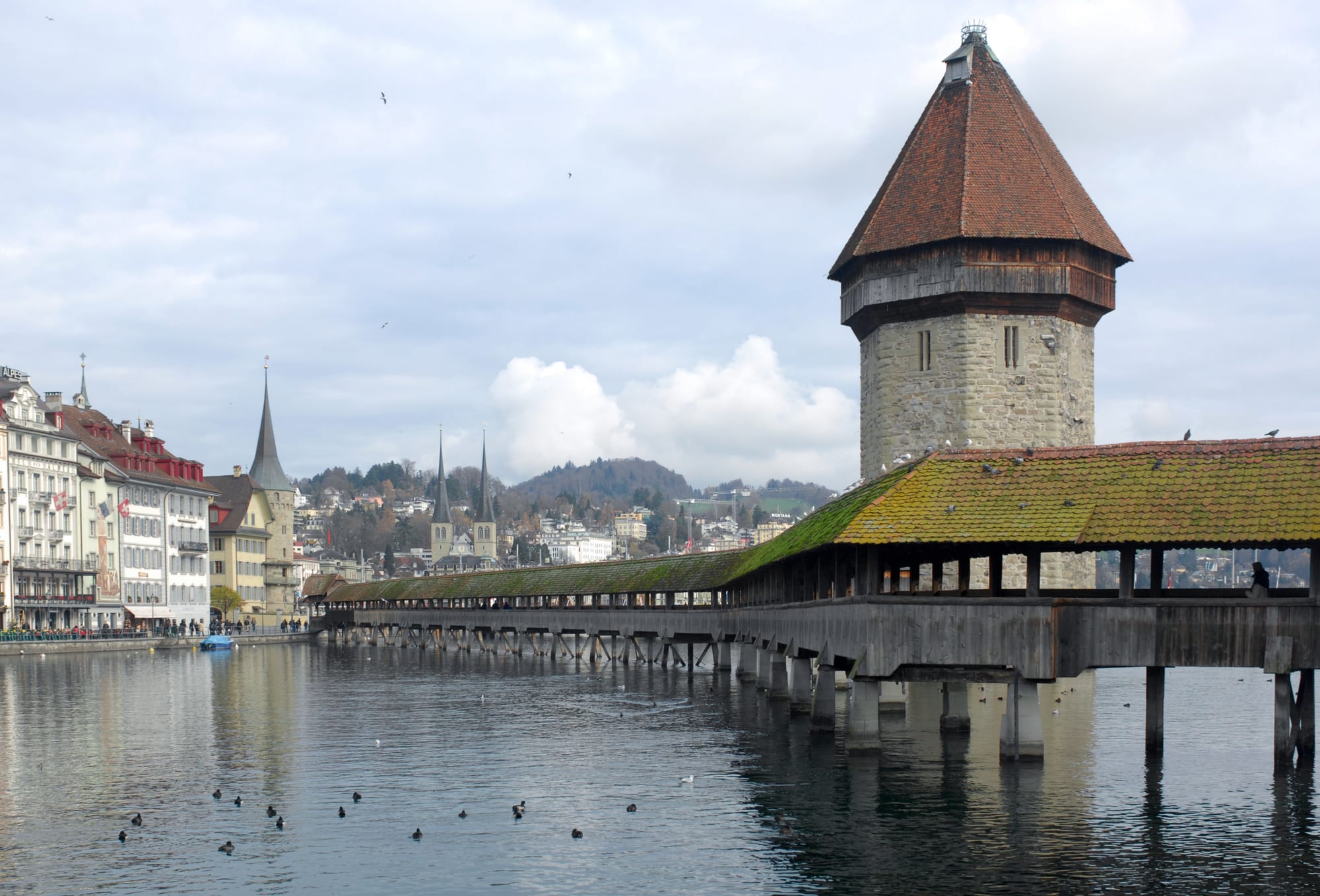 A historic covered wooden bridge crossing a river beside a tower