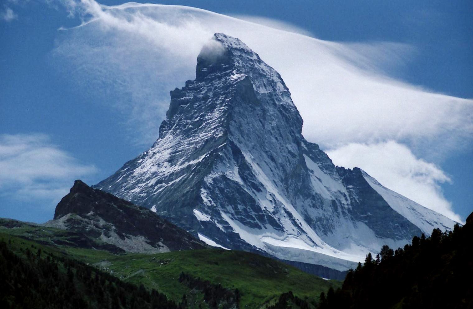 A dramatic snow-covered pyramid-shaped peak with a cloud streaming off its summit