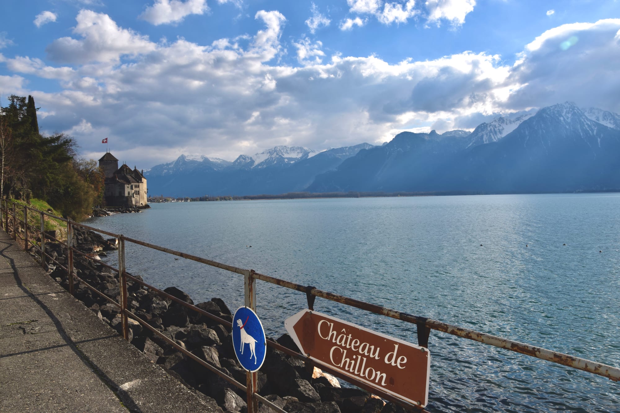 A medieval lakeside castle with turrets, seen across water with mountains behind