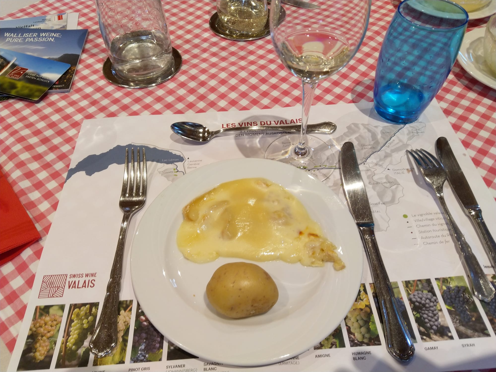 A plate of melted cheese with potatoes and a glass of wine