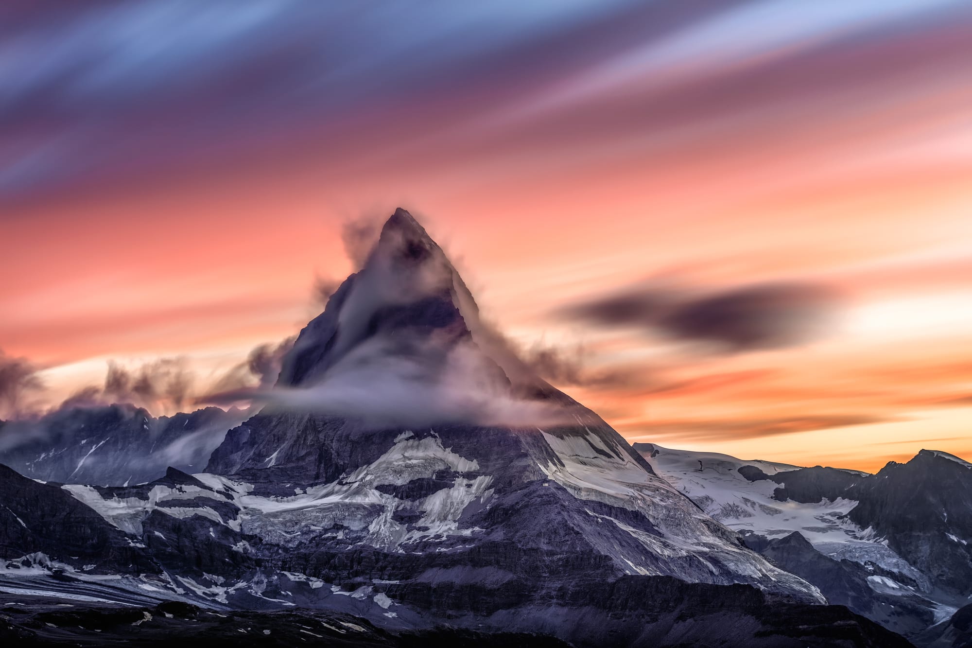 The pyramidal peak of the Matterhorn glowing pink at sunset above dark alpine ridges