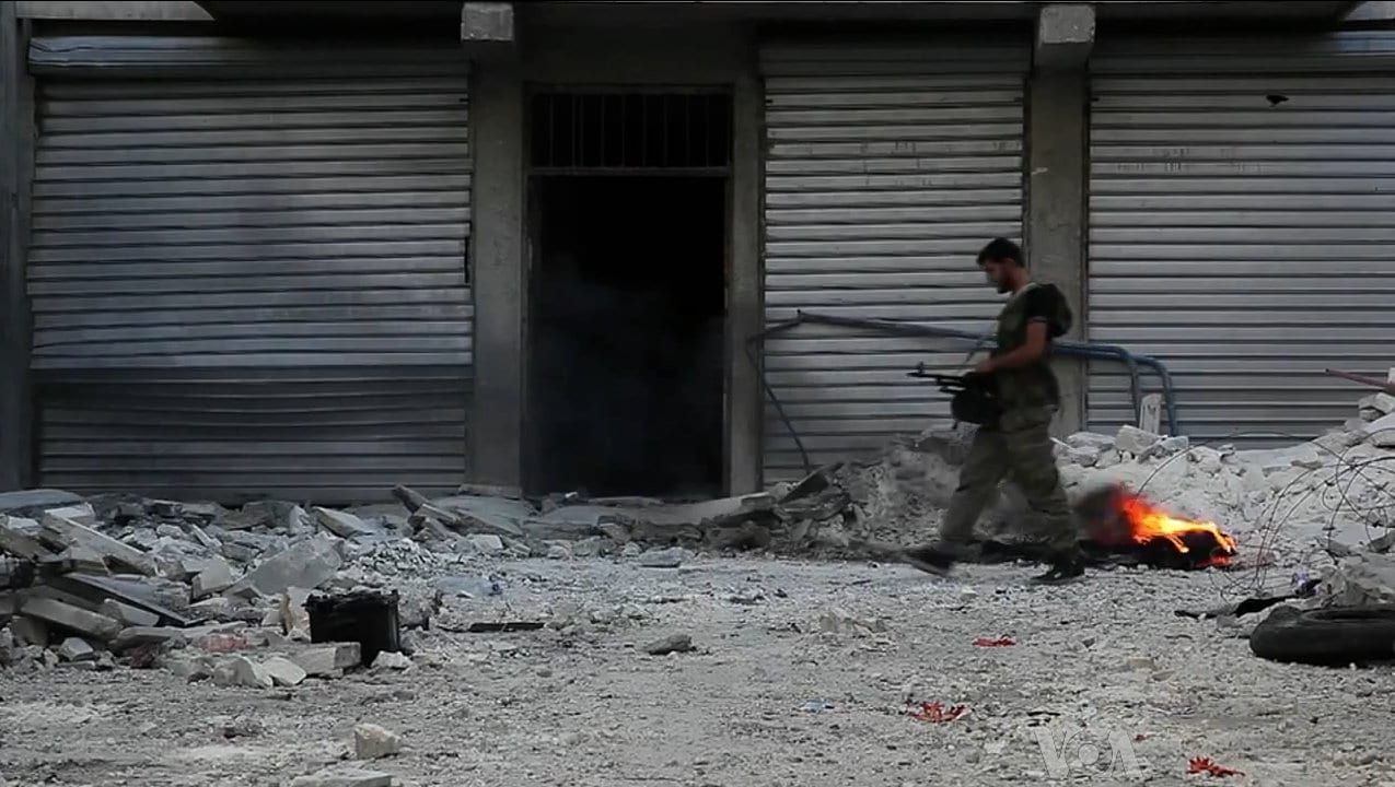 An armed fighter walking through a street of gutted, rubble-strewn buildings in Aleppo