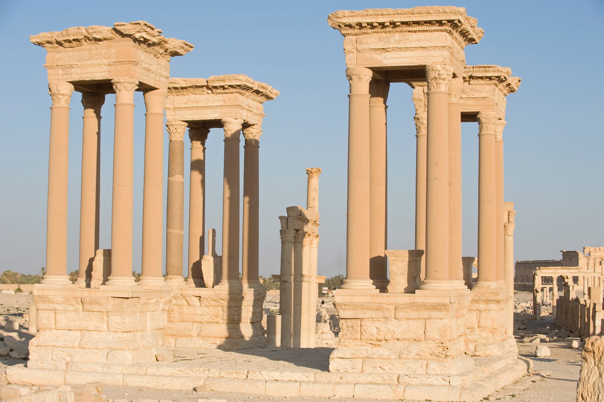 Four groups of tall stone columns on raised platforms, each topped with a carved entablature, standing in the desert ruins of Palmyra