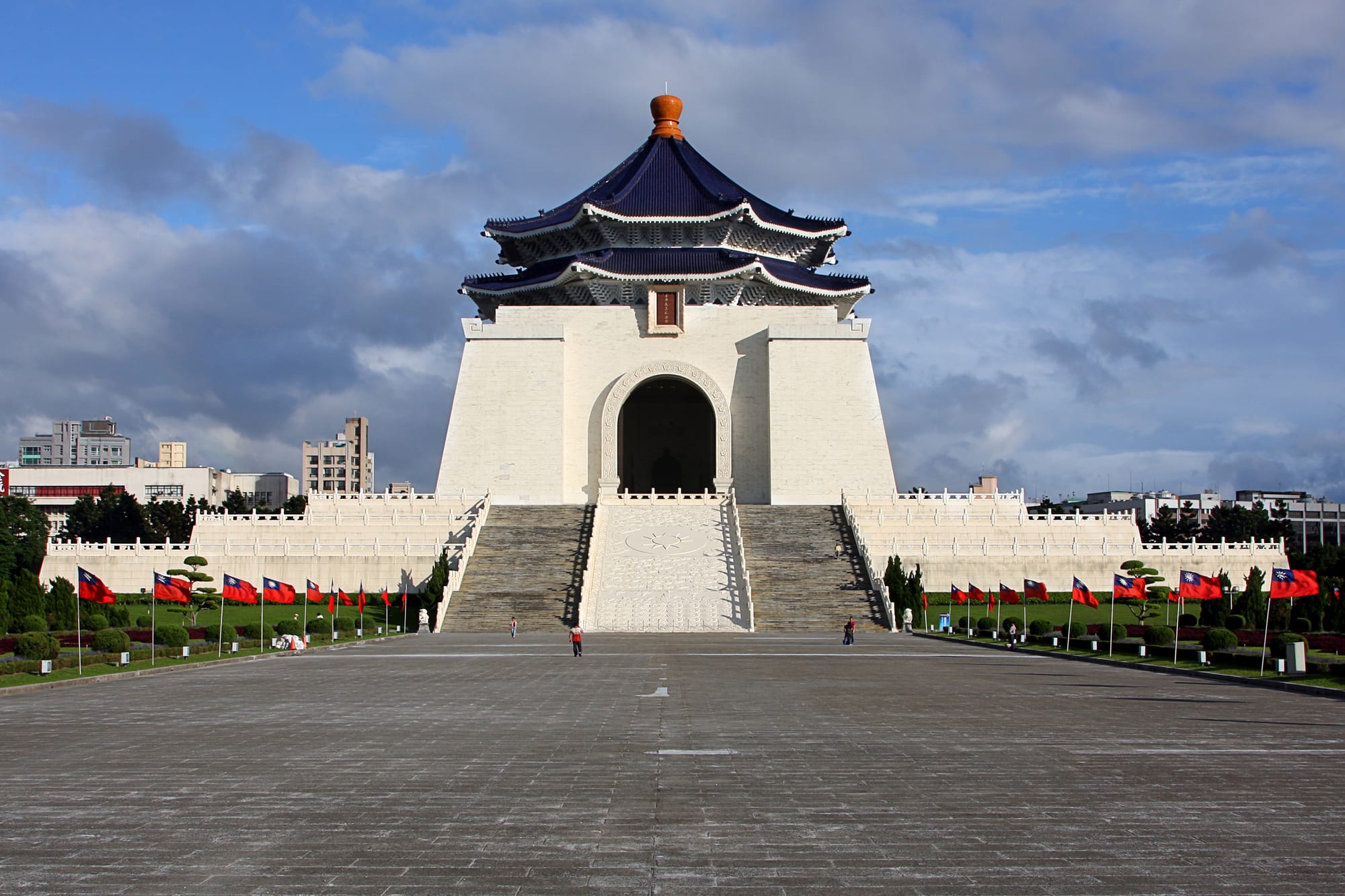 A large white memorial hall with a blue tiled roof on a grand plaza