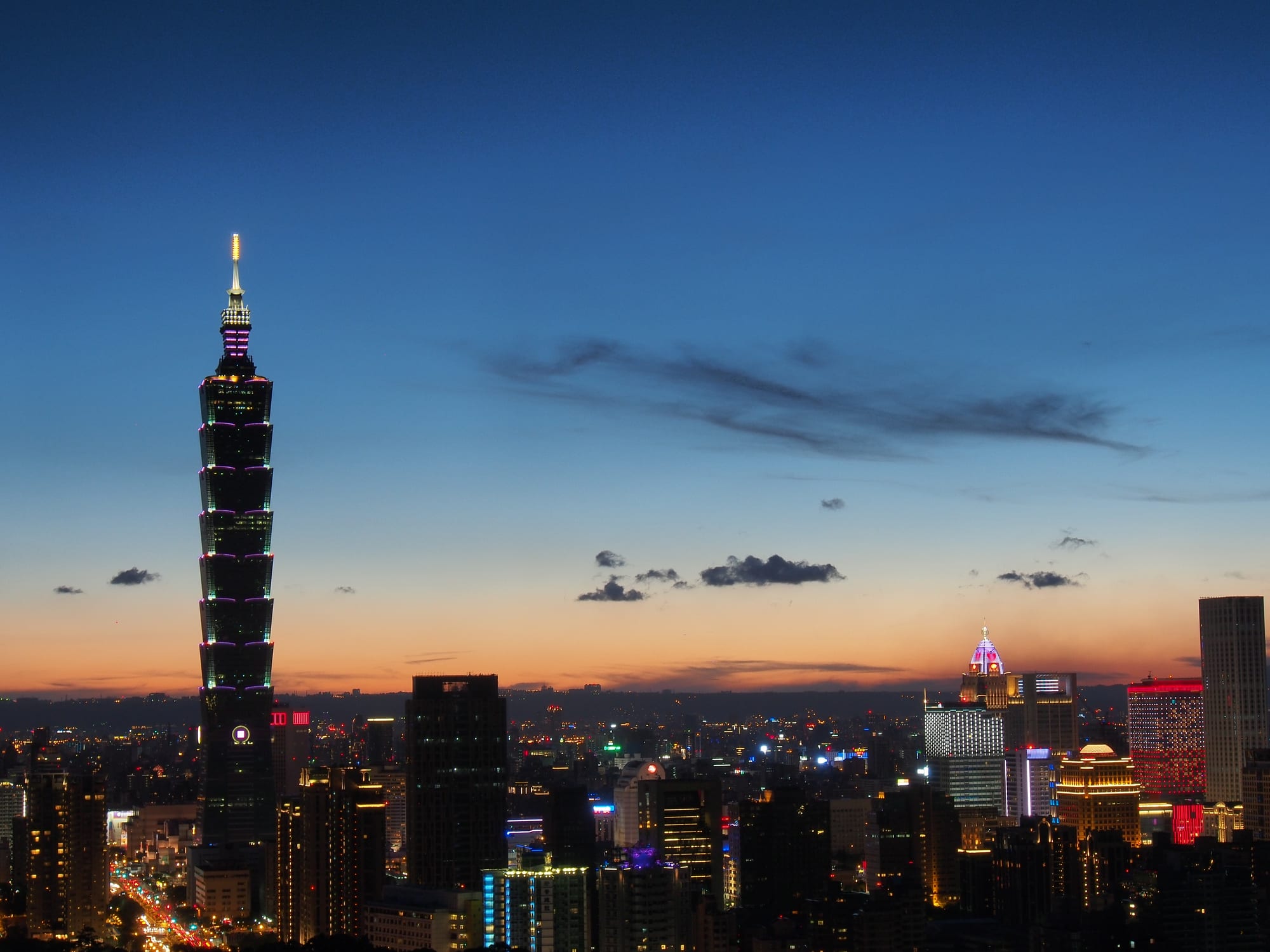 A tall segmented skyscraper illuminated at dusk in a city skyline