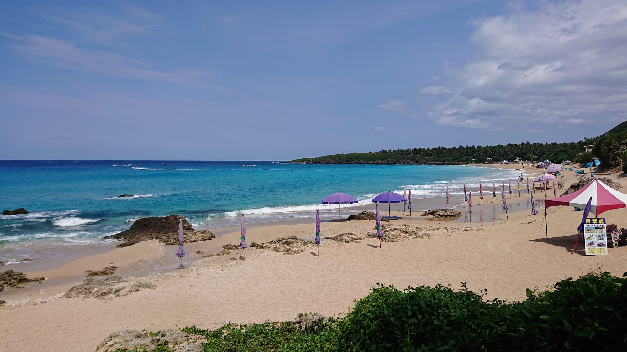 A turquoise bay with beach umbrellas along a sandy shore backed by hills