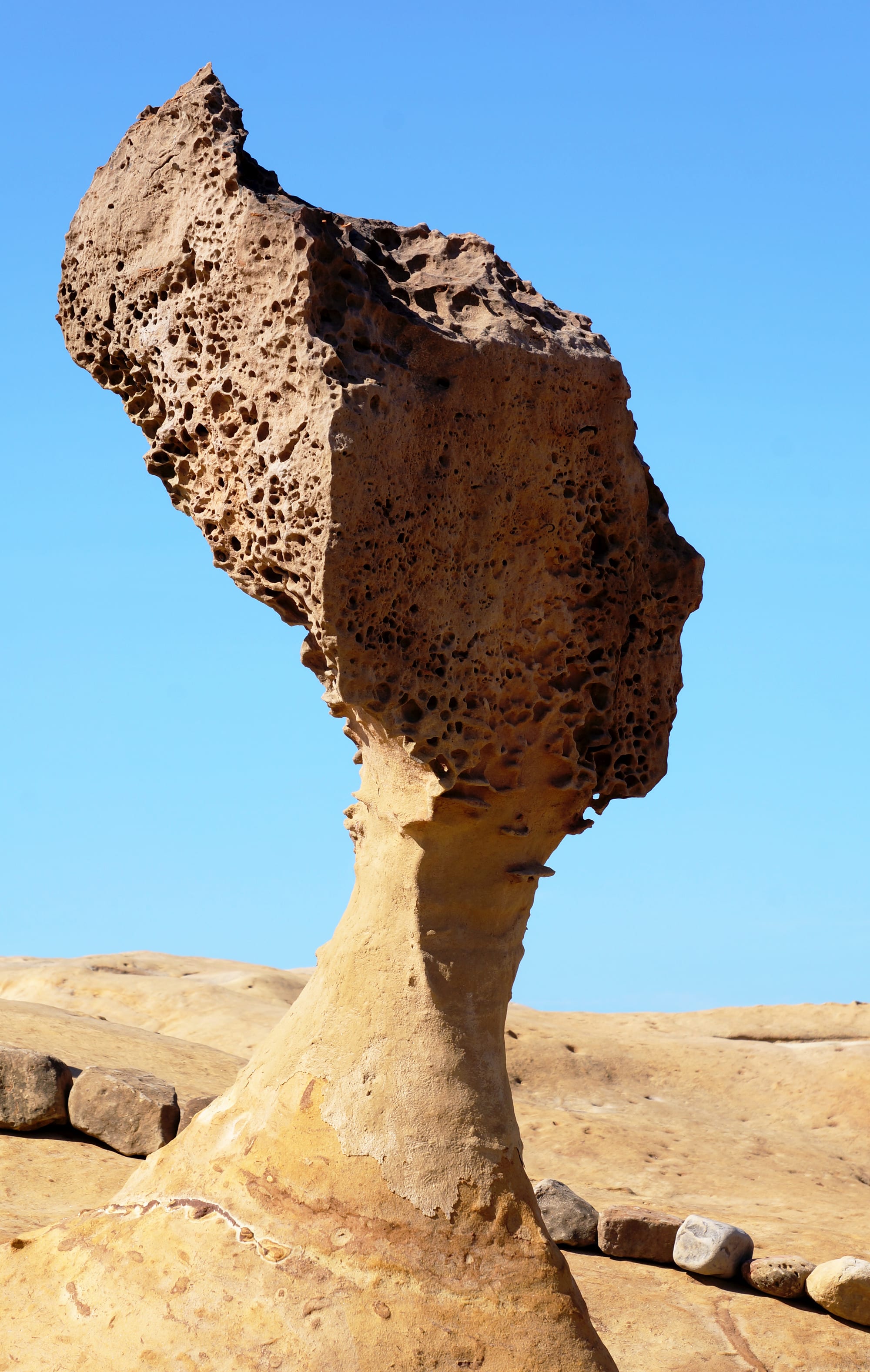 A mushroom-shaped rock formation balanced on a narrow eroded base above a rocky coastline