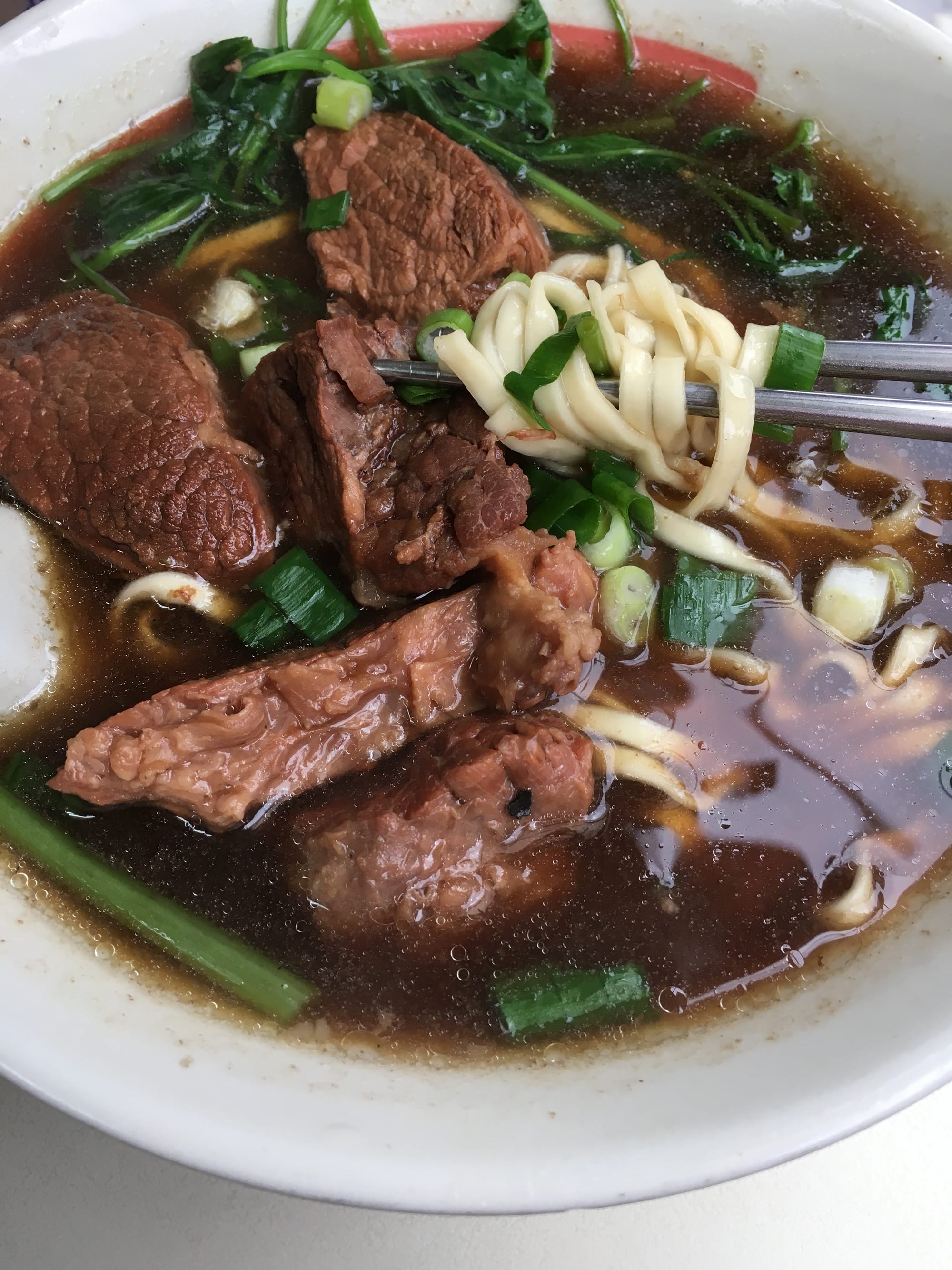 A bowl of noodle soup with beef and broth