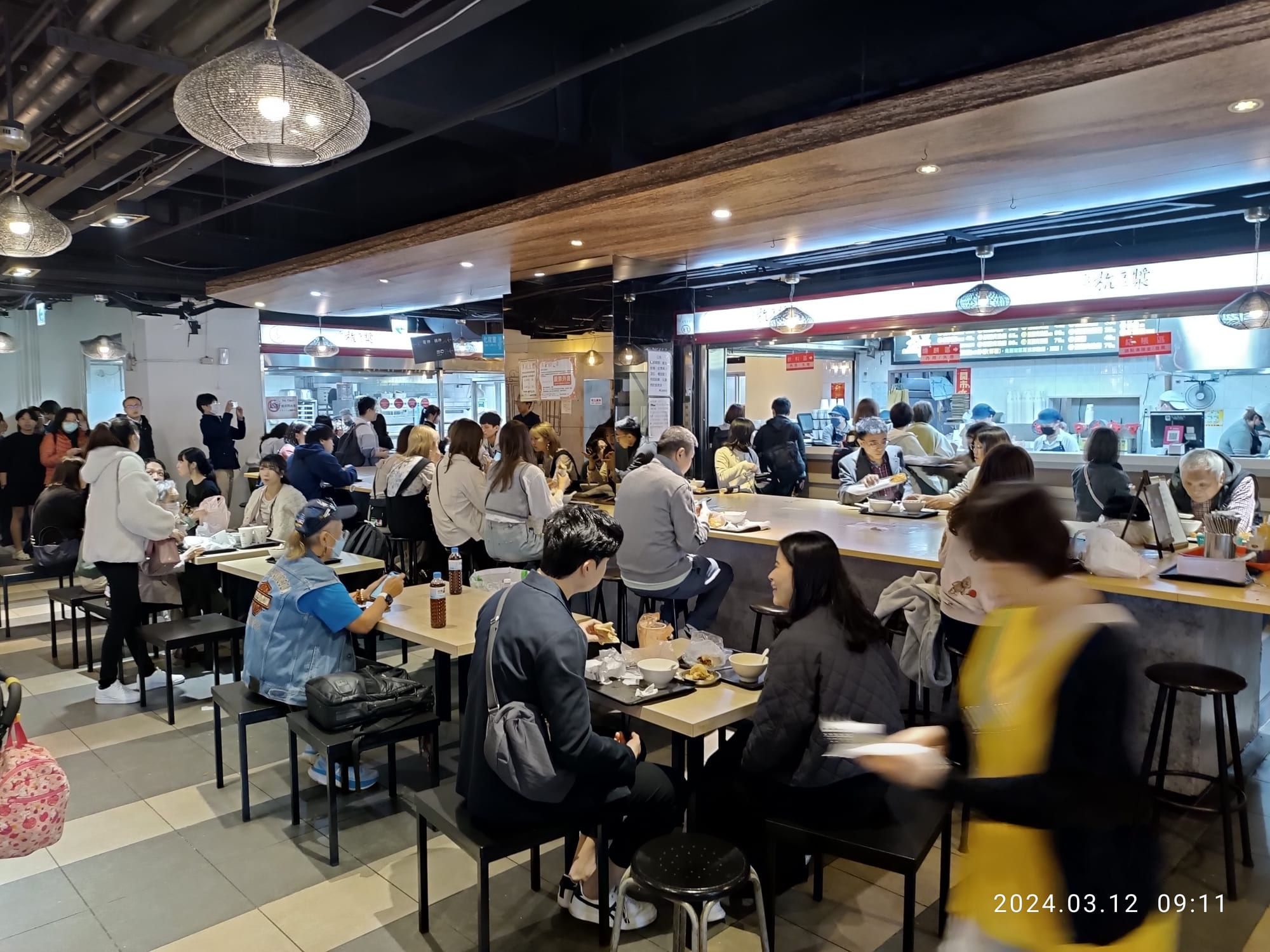 A crowded indoor breakfast food court in Taipei with people queuing and eating at shared tables