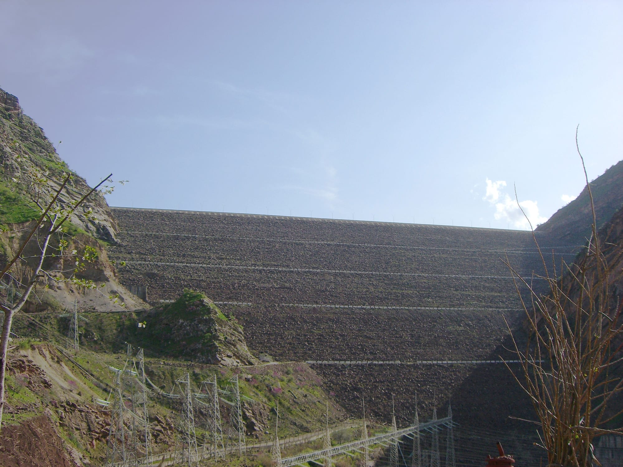 A massive earth-fill dam wall holding back a reservoir in a steep mountain valley
