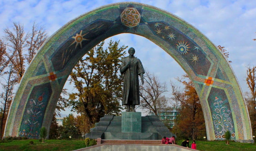 A formal park with fountains and a large golden monument leading to a government building in Dushanbe