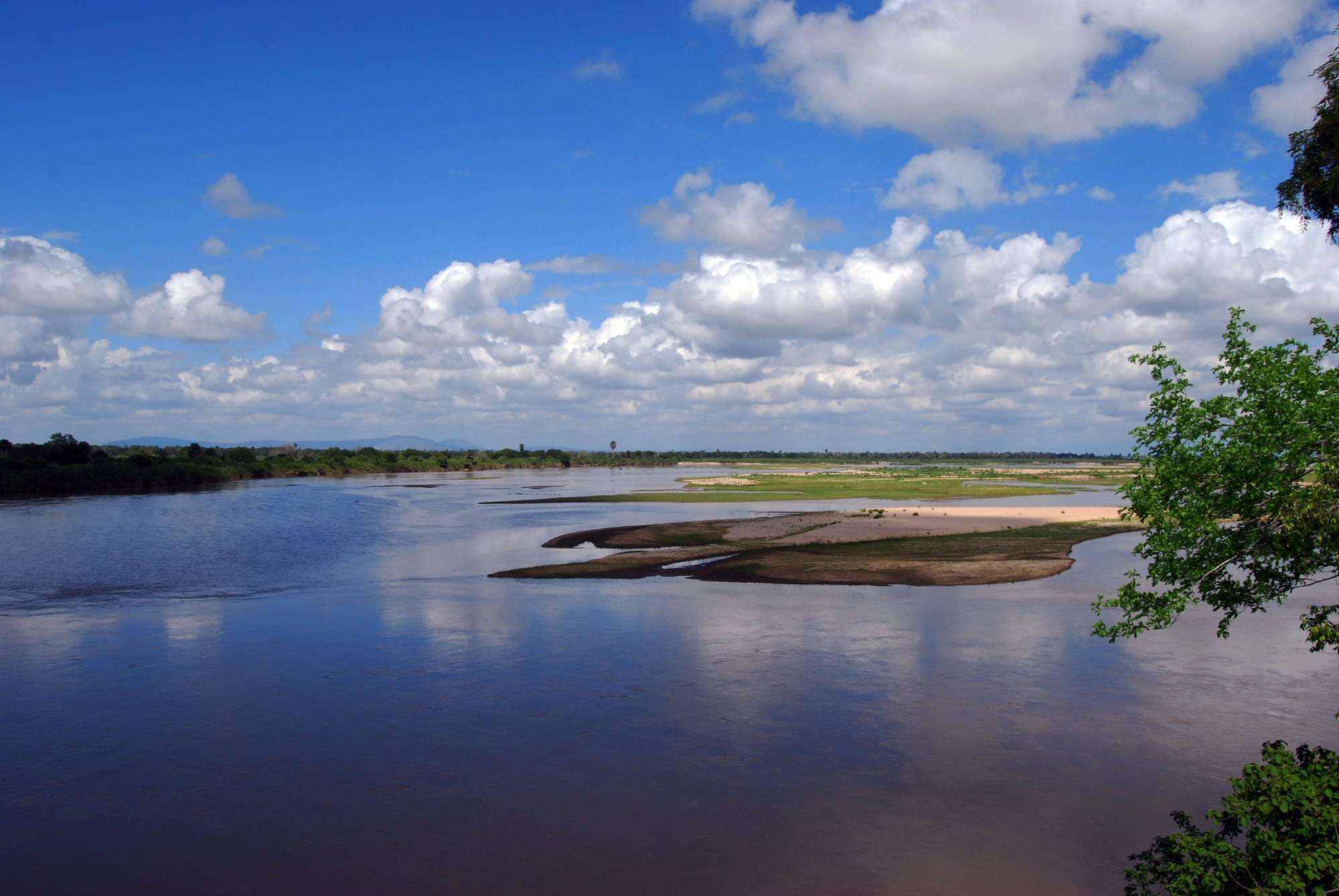 A wide, calm river with sandbanks and riverine forest under a partly cloudy sky