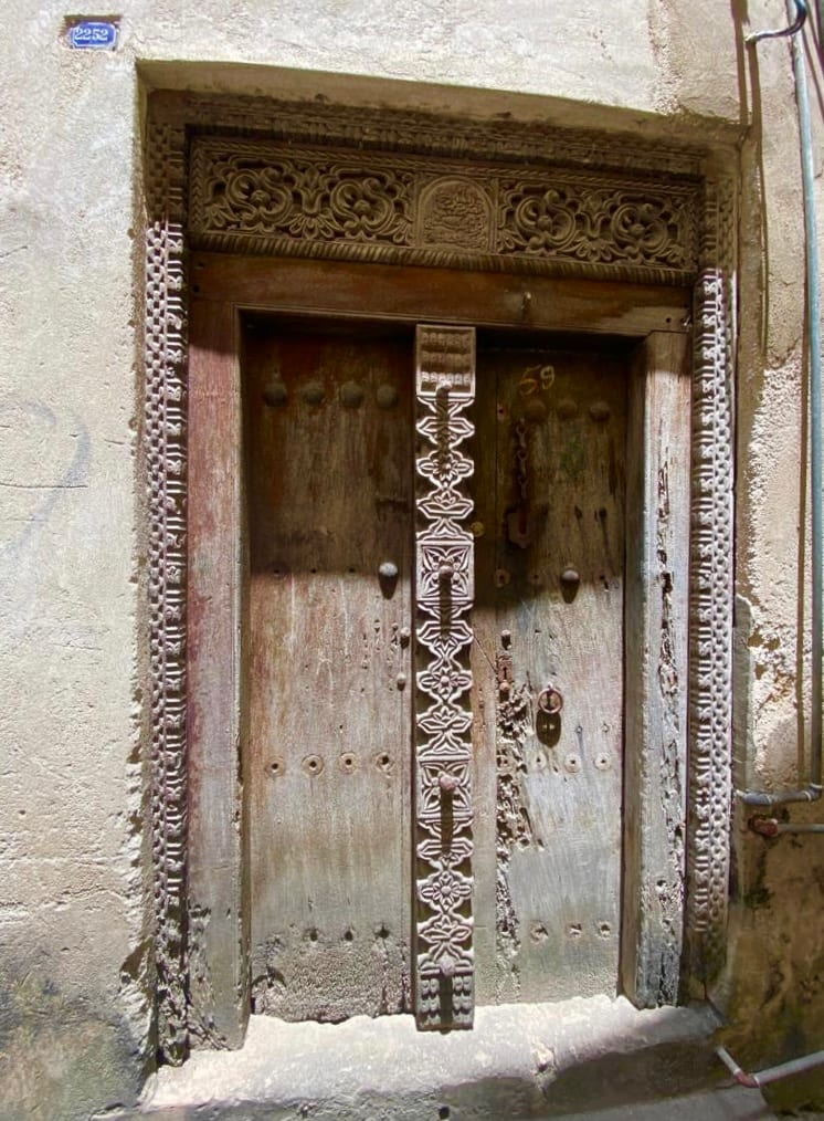 An ornately carved wooden door with brass studs set in a coral-stone wall in Stone Town, Zanzibar