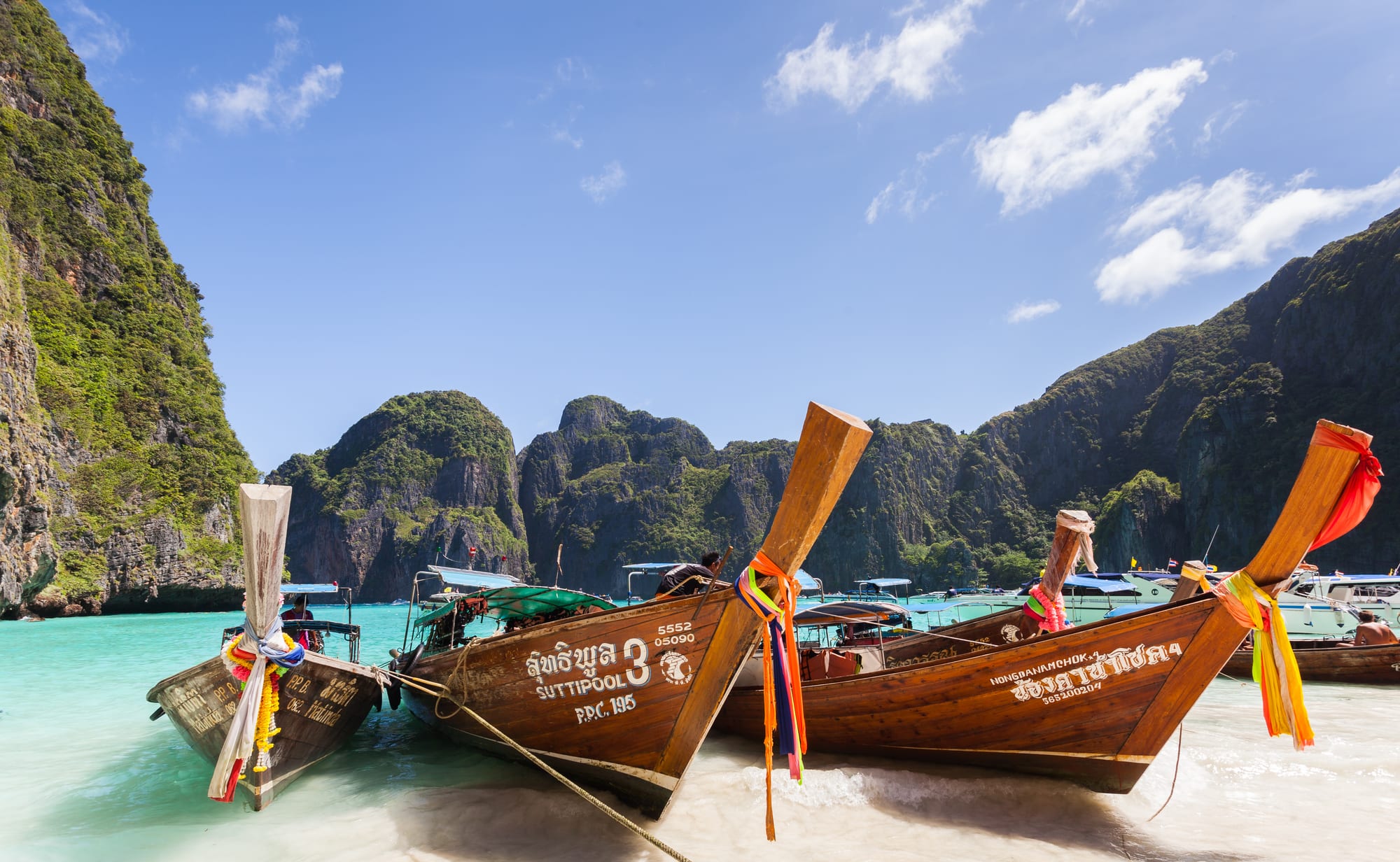 A crowded turquoise bay surrounded by dramatic limestone cliffs