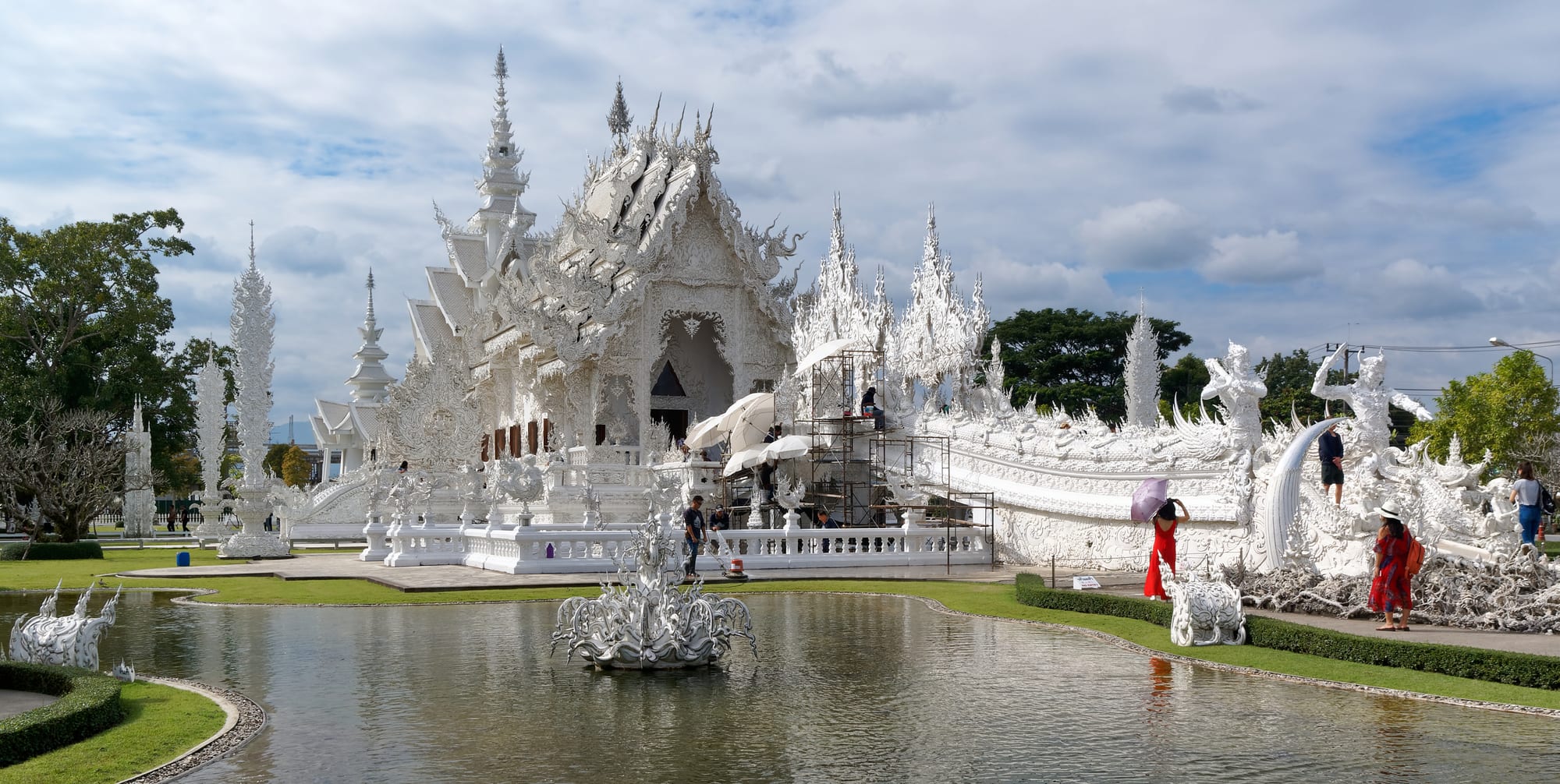 An elaborate white temple complex with intricate silver spires, reflected in a pool