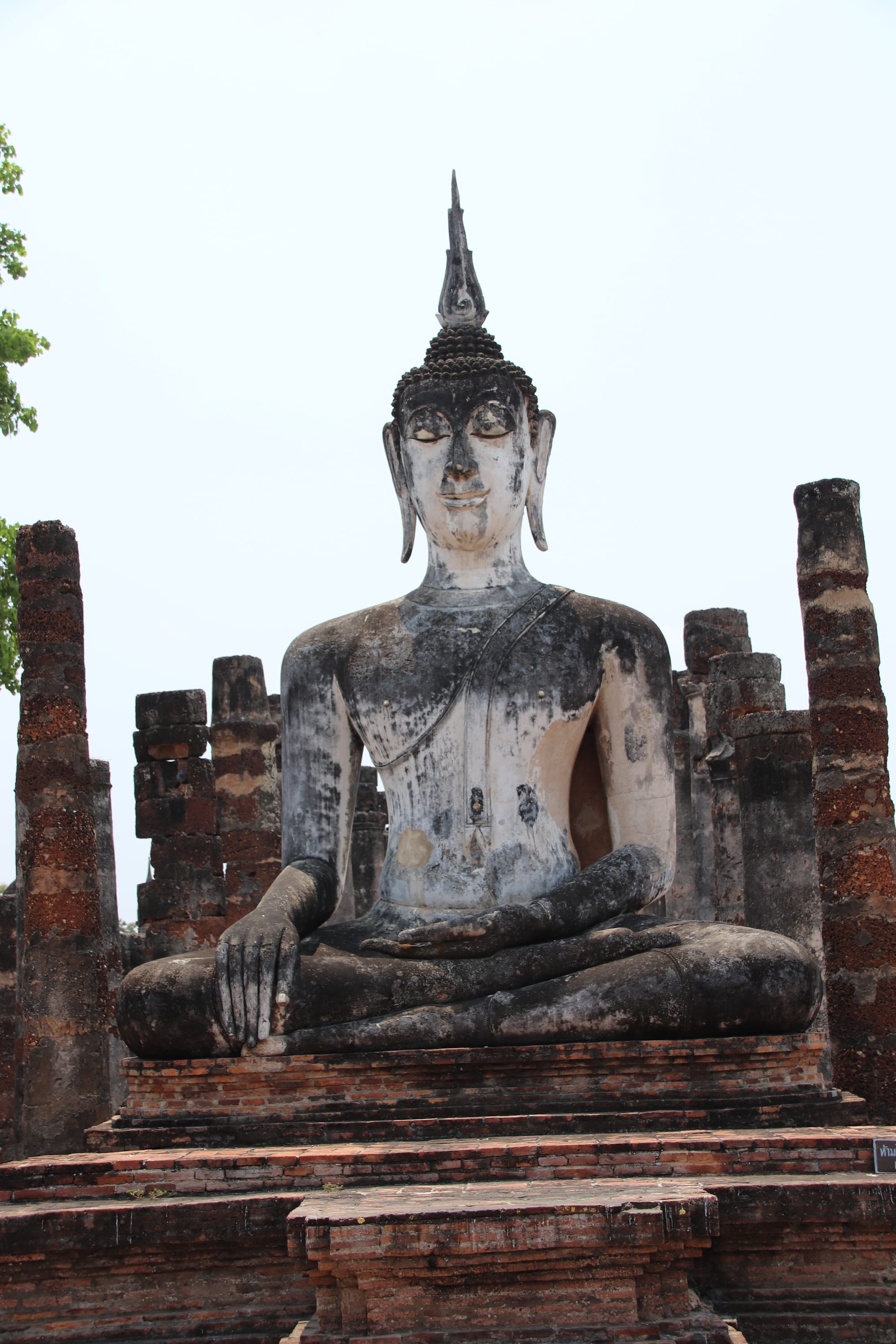 A weathered stone Buddha statue seated among ruined brick temple columns