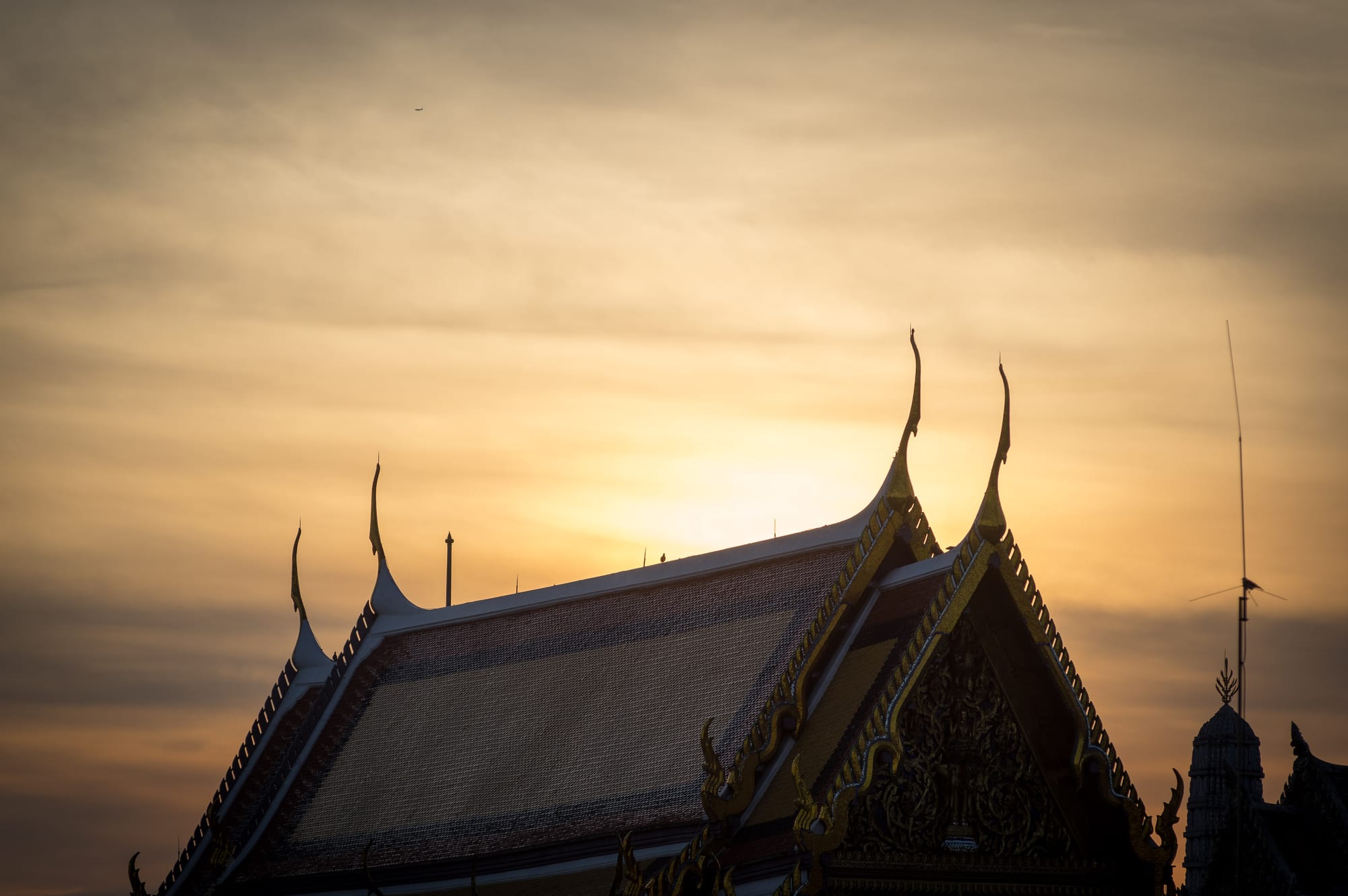 The gilded, multi-tiered roofs and spires of the Grand Palace complex in Bangkok glowing at sunrise