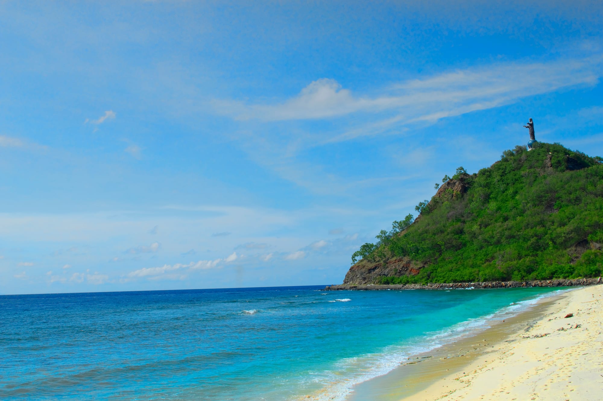 A palm-lined white sand beach along a calm bay