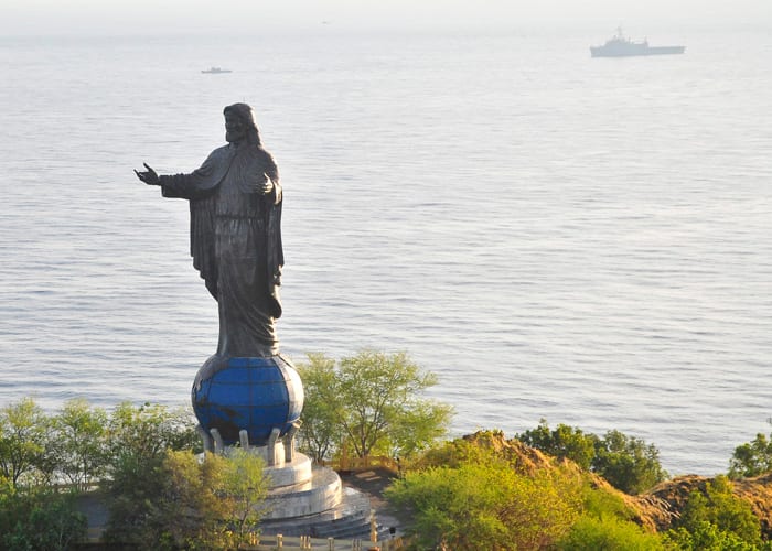 A large statue of Christ standing on a hilltop overlooking the sea