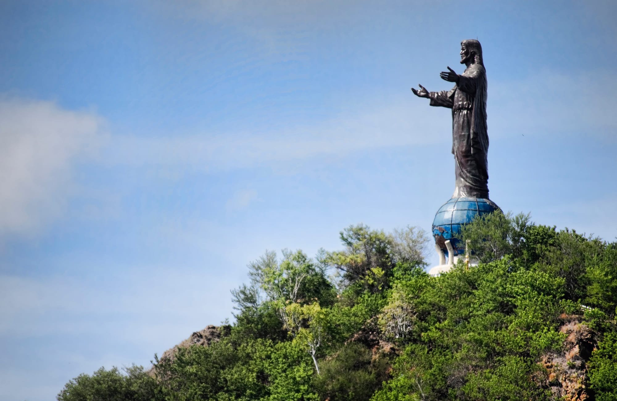 A tall white statue of Christ with arms outstretched on a headland above a blue bay near Dili