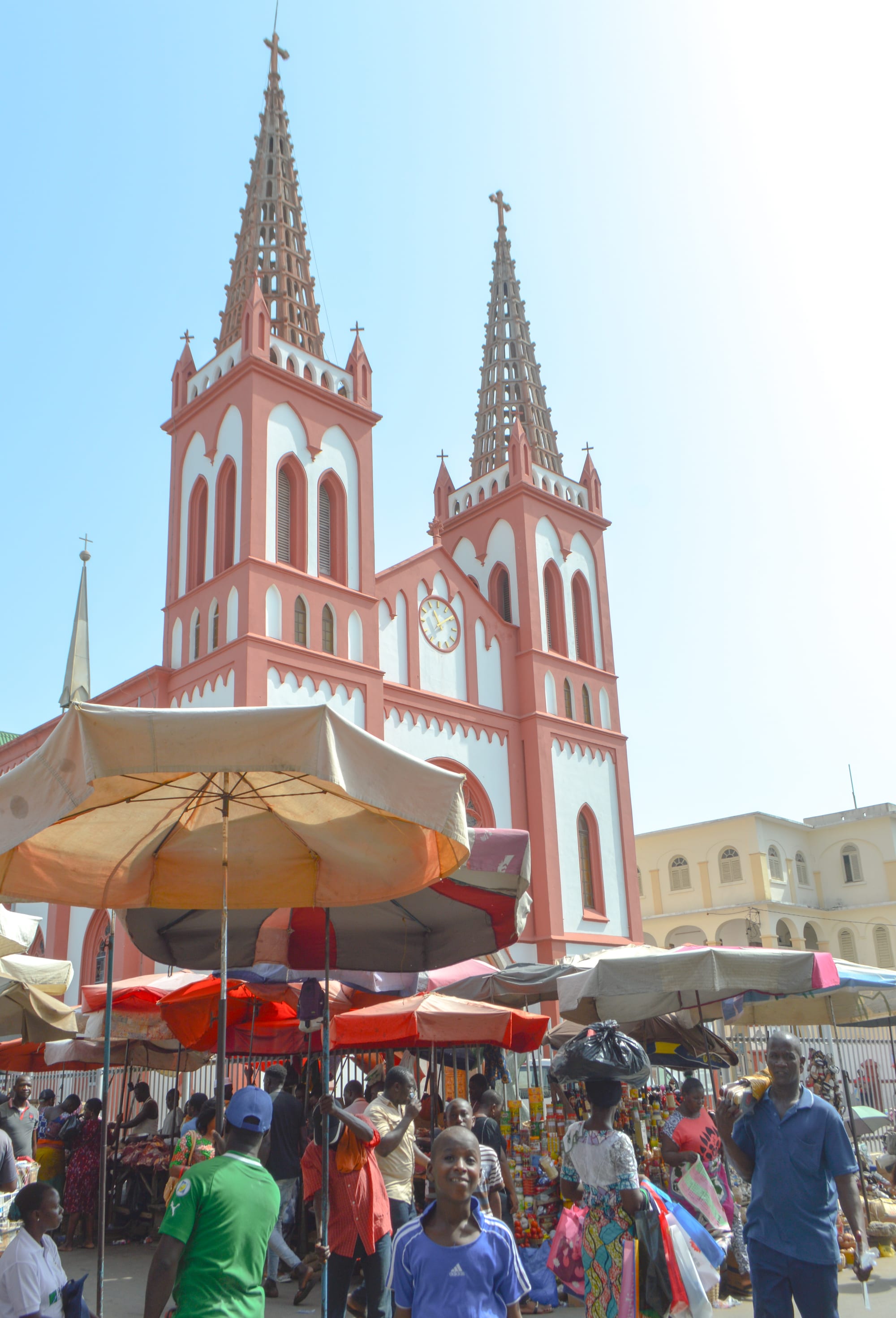 A pink-and-white twin-spired cathedral rising above busy vendor umbrellas and shoppers in a Lomé market