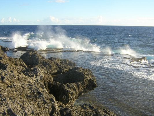 Ocean waves erupting through coastal rock formations along a shoreline