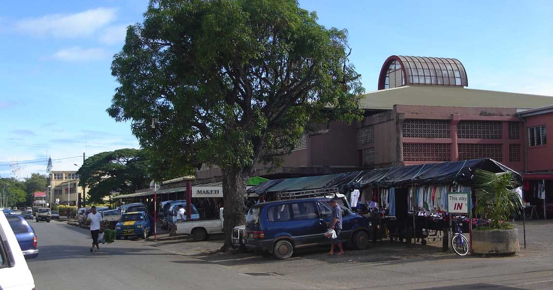 The Talamahu Market building in Nuku'alofa, with covered stalls, parked cars and shoppers on the street outside