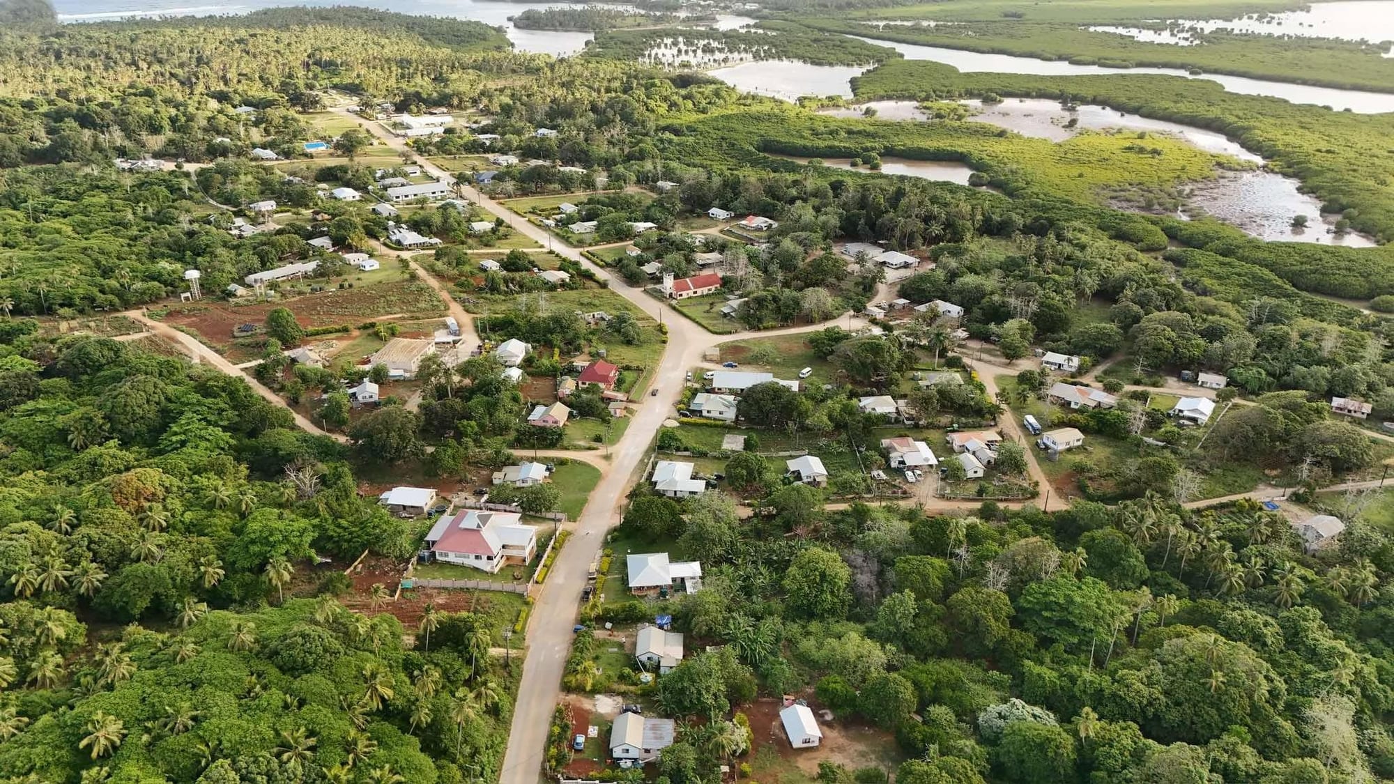Aerial view of Tuʻanekivale village in Vavaʻu, Tonga, showing houses along cross-shaped roads surrounded by forest and a lagoon