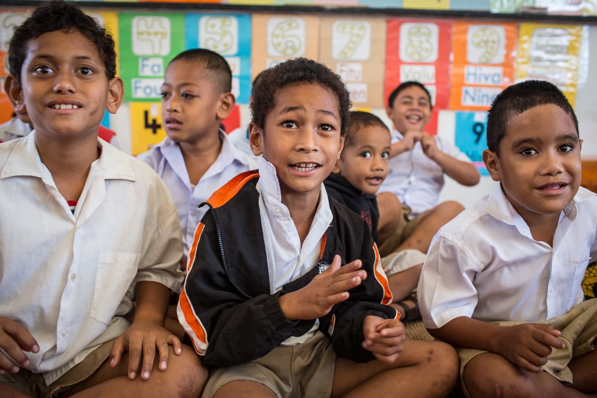 Tongan primary school children in white uniform shirts sitting together in a classroom, smiling and engaged