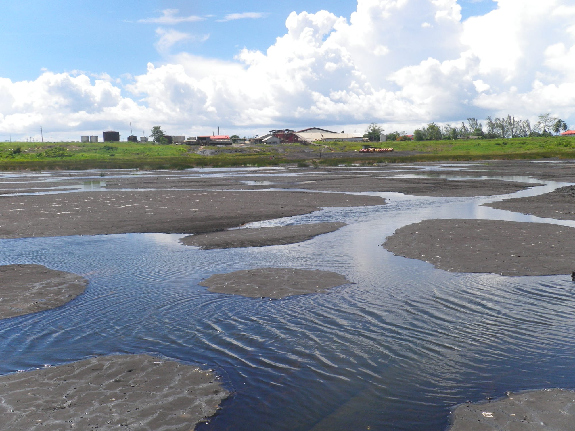 A vast dark expanse of natural asphalt with pools of water on its surface