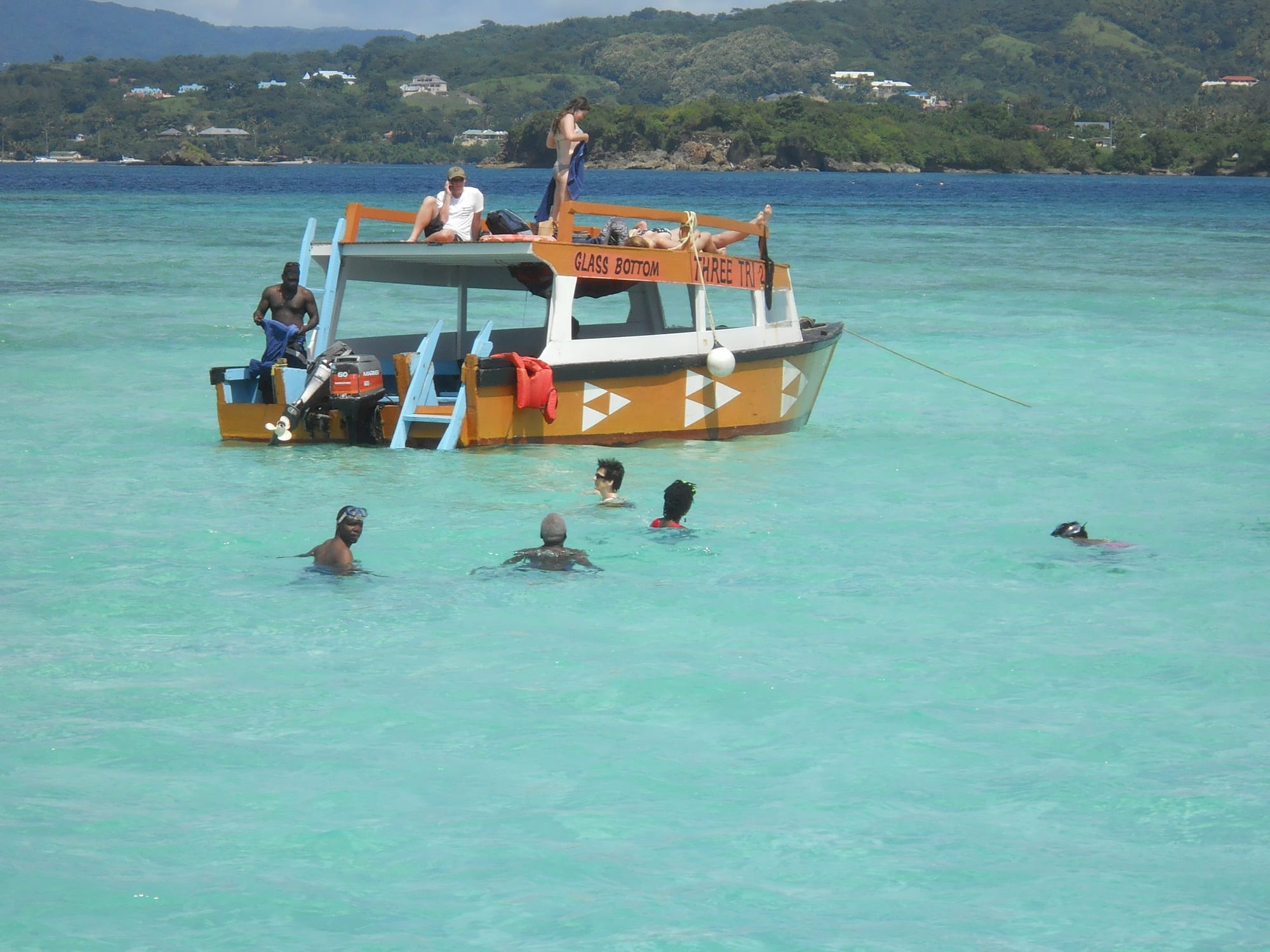 Swimmers and a glass-bottom boat in a shallow turquoise sandbank pool