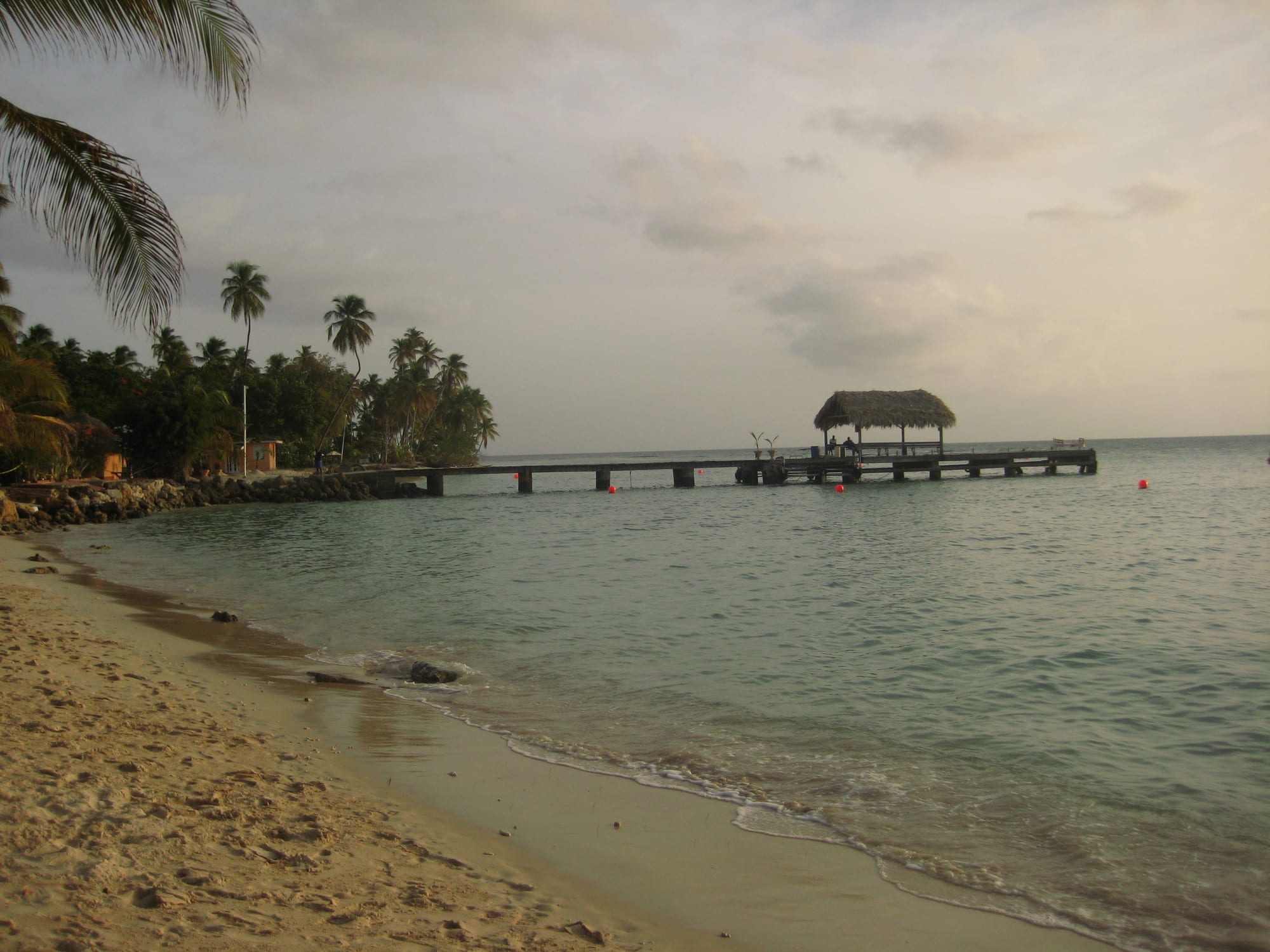 A thatched-roof jetty extending into calm turquoise Caribbean water